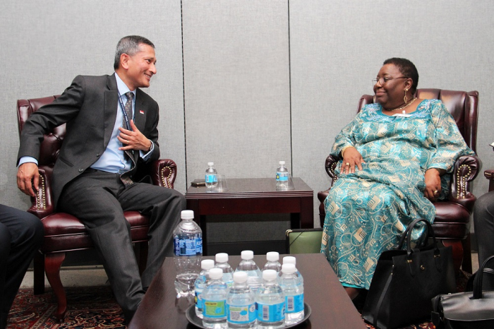 Two people in business attire sit in chairs facing each other in front of water bottles.
