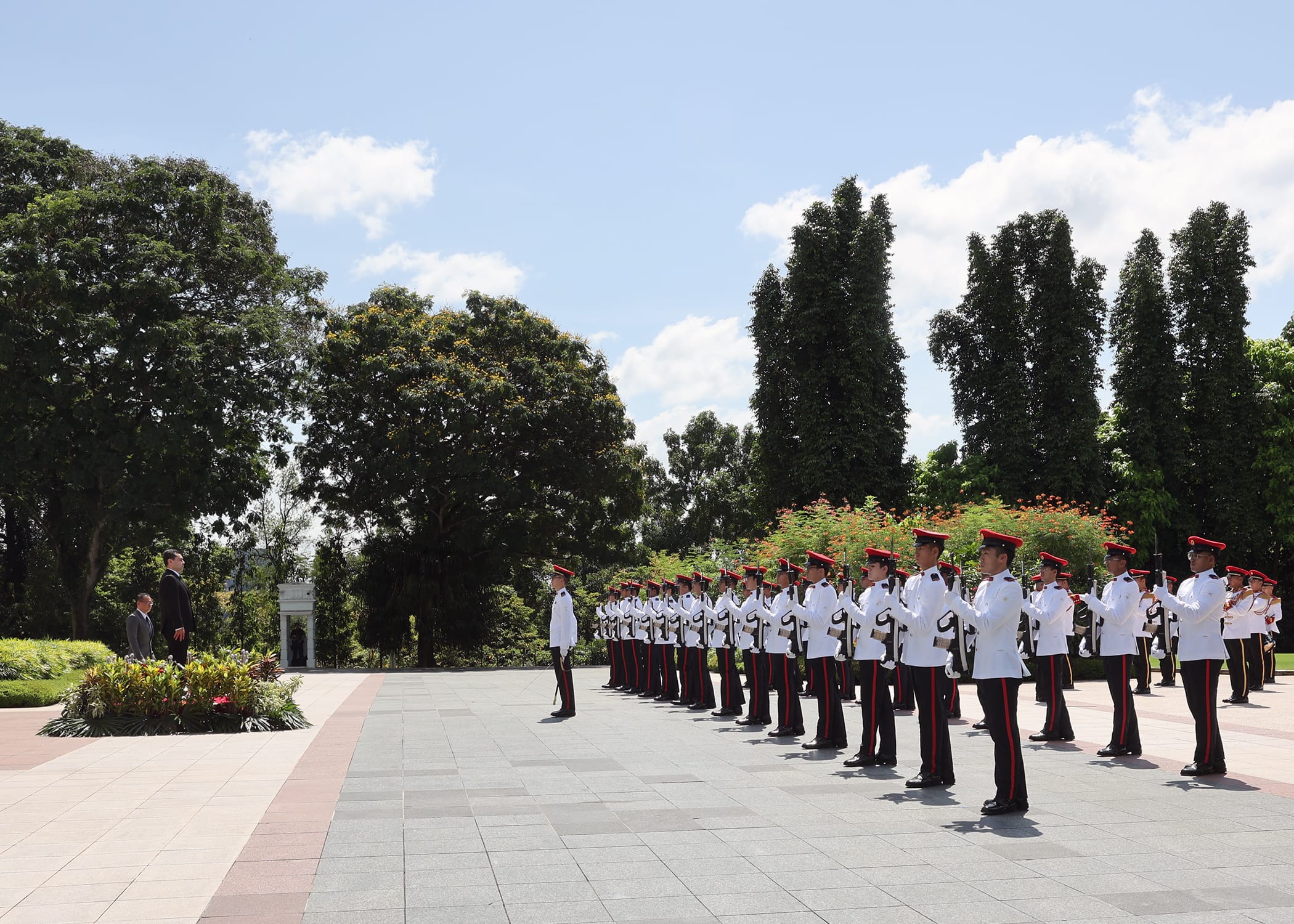 Honor guard in red hats and white uniforms stand at attention. Man in dark suit watches.