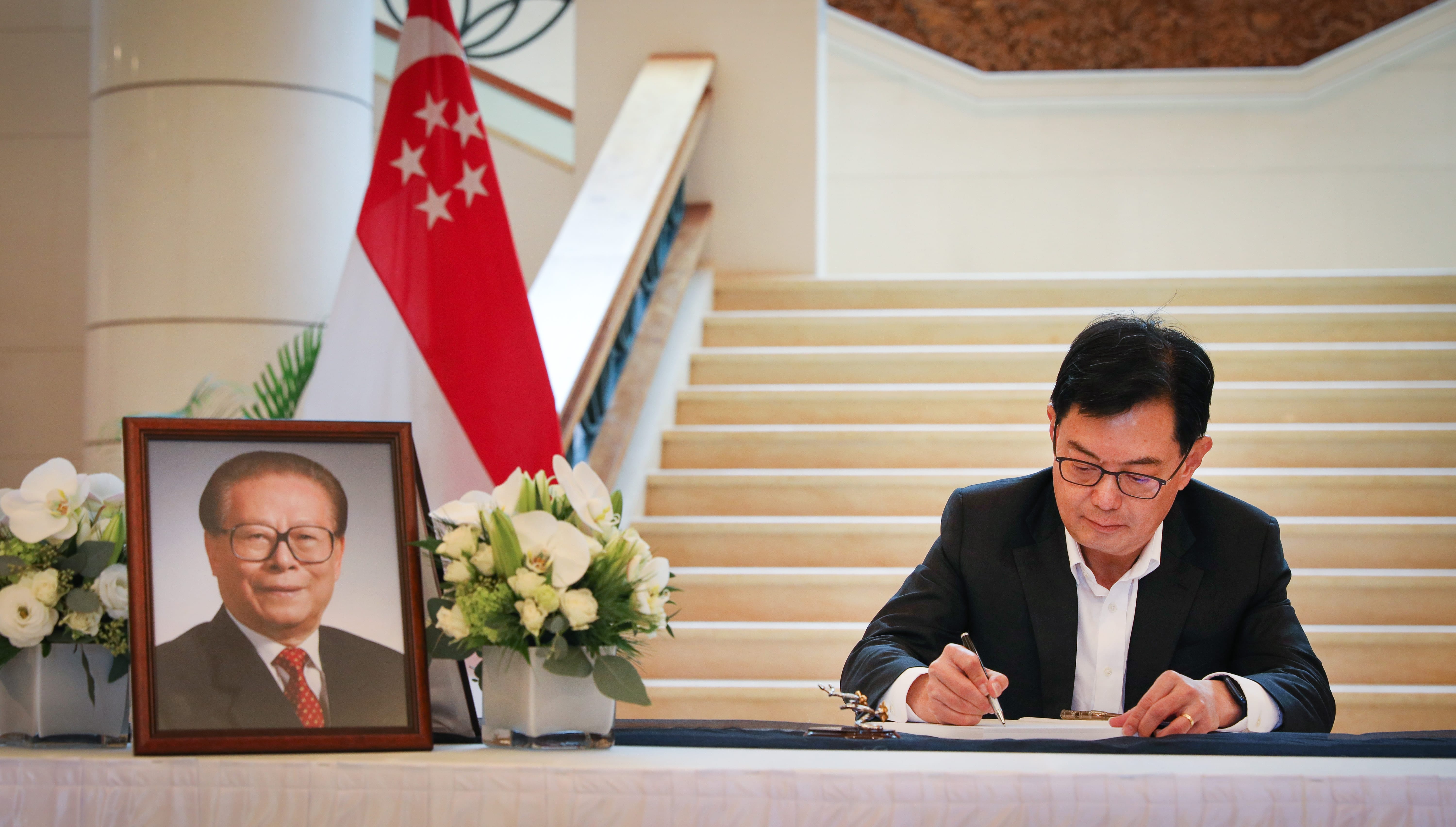People seated at a long table, with drinks and menus. Floral arrangements center table.