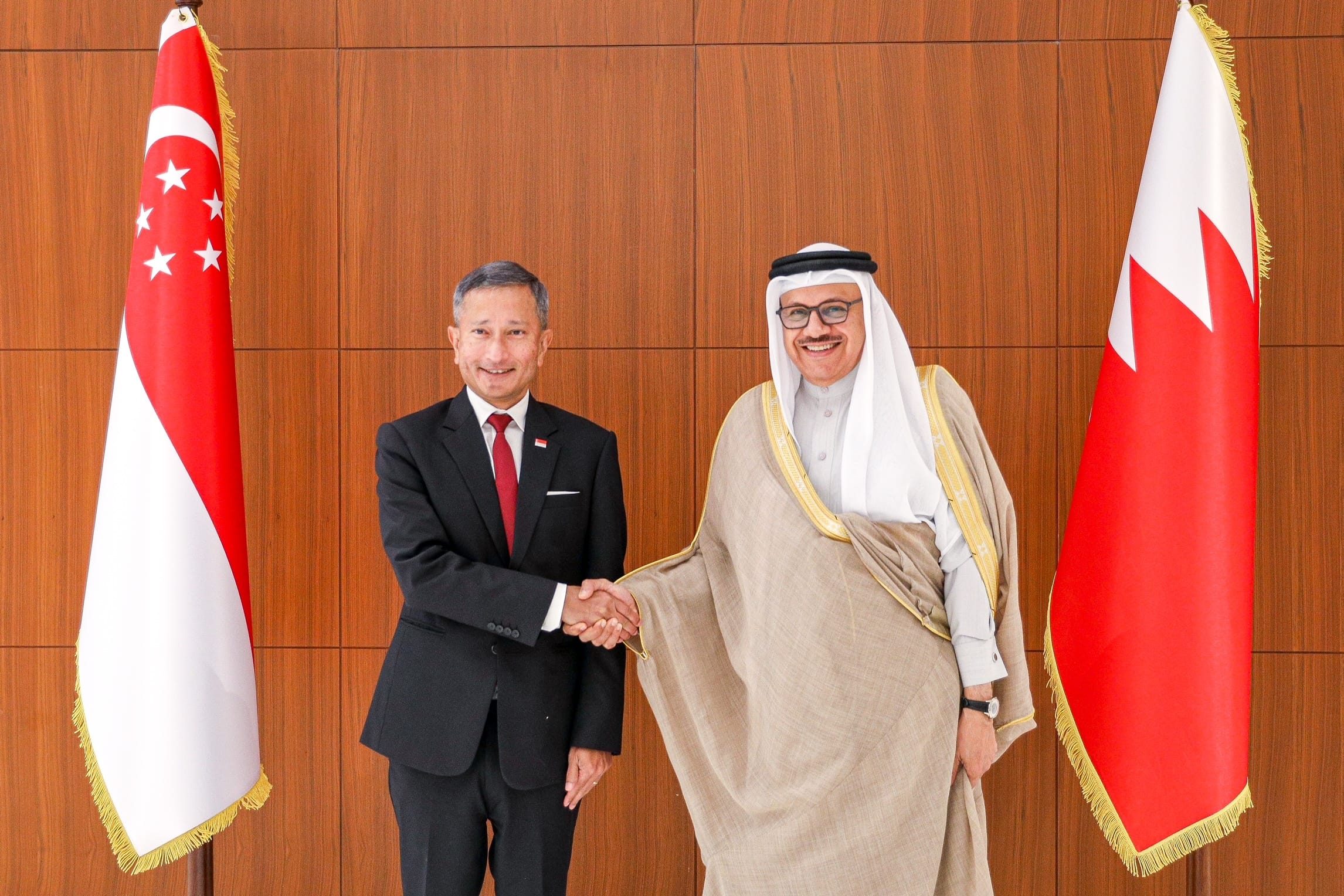 Two men shaking hands between the Singapore and Bahrain flags.