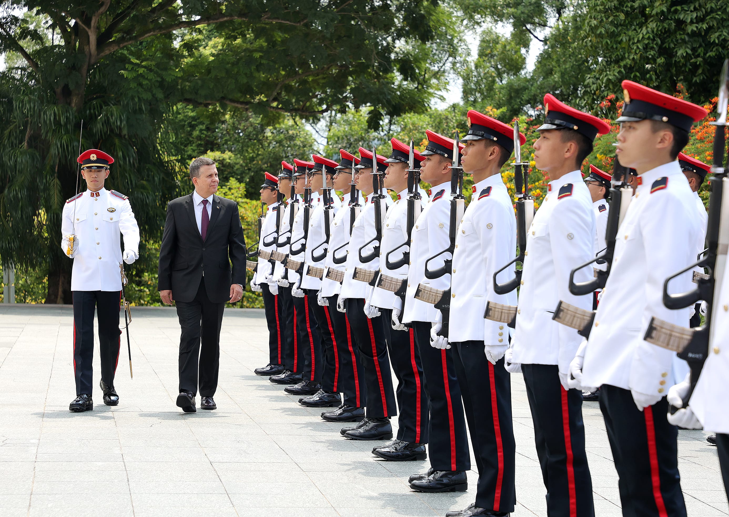 Soldiers in formation in white uniforms with red caps and a man in a dark suit.
