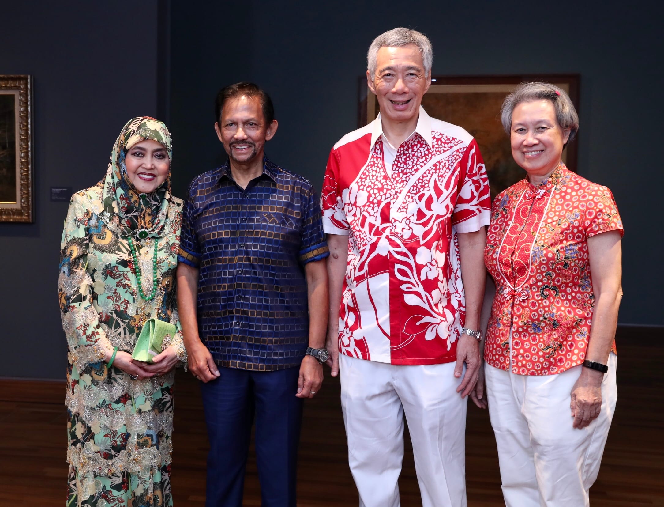 Four people stand in front of artwork, dressed in patterned clothing. Lee Hsien Loong is on the right.