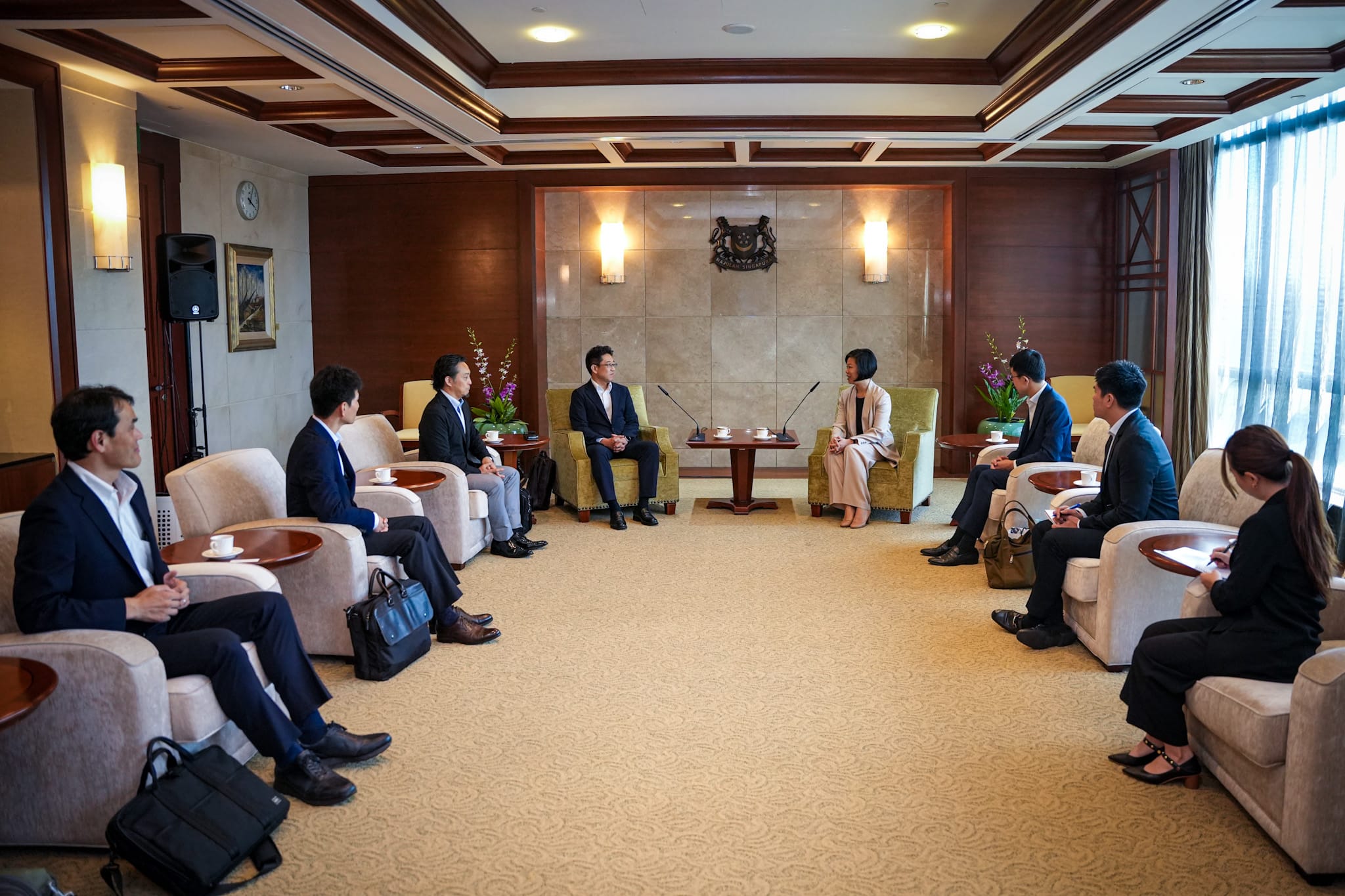 People in business attire sitting for a meeting in a formal conference room.