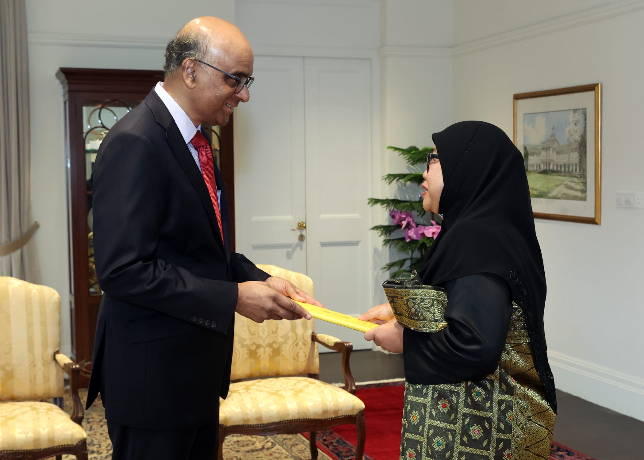Halimah Yacob presents a yellow folder to a man in a suit.