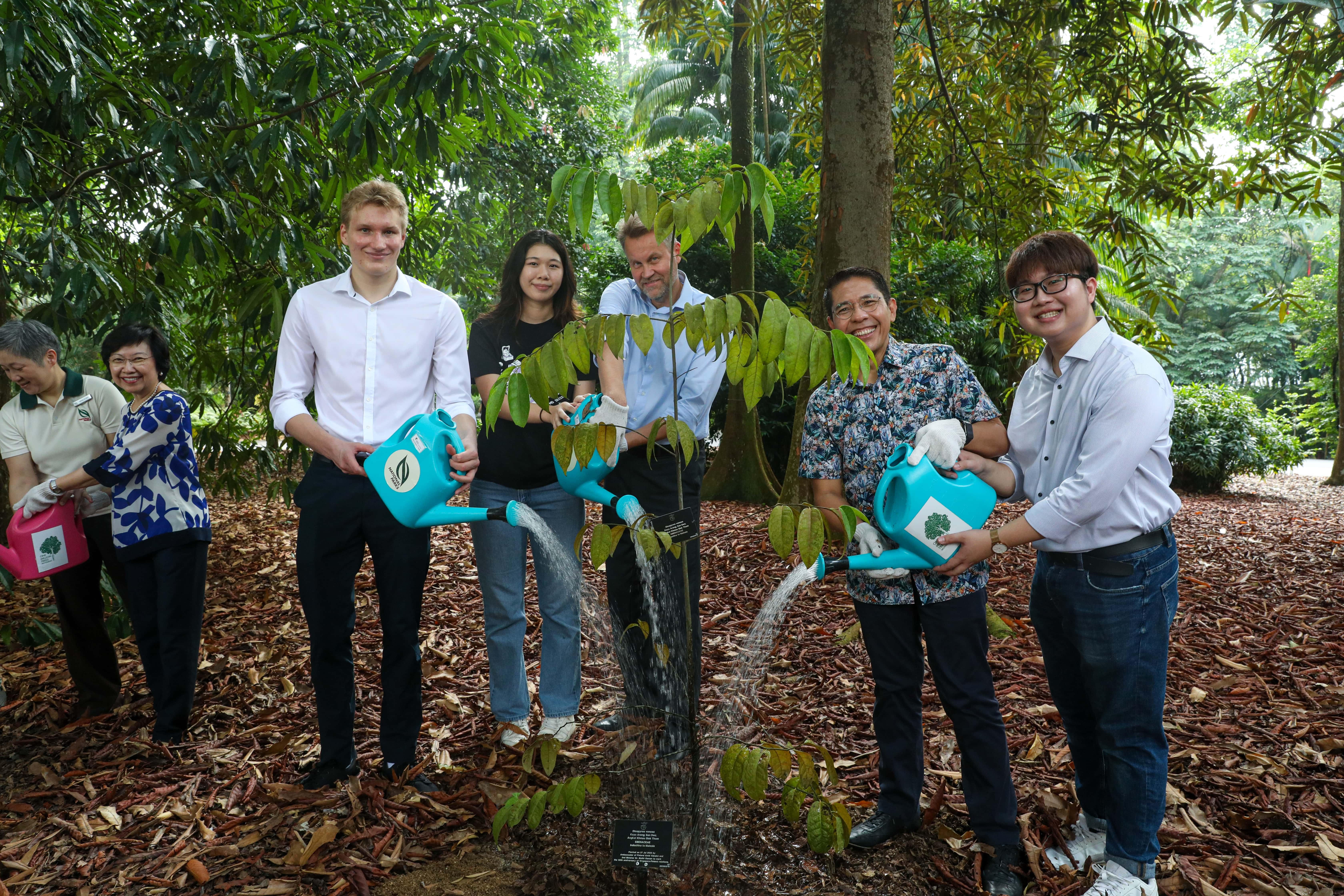 Group of people posed on a red carpeted staircase with white railing, with floral arrangements.
