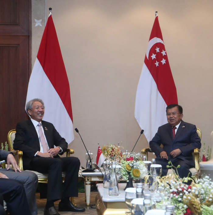Two men in suits seated with Indonesian and Singapore flags behind them.