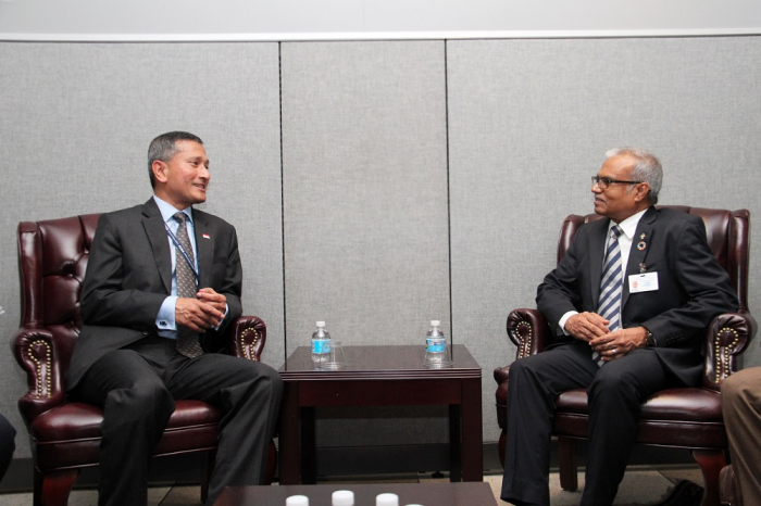 Two men in suits seated in leather chairs, facing each other, with water bottles on table.