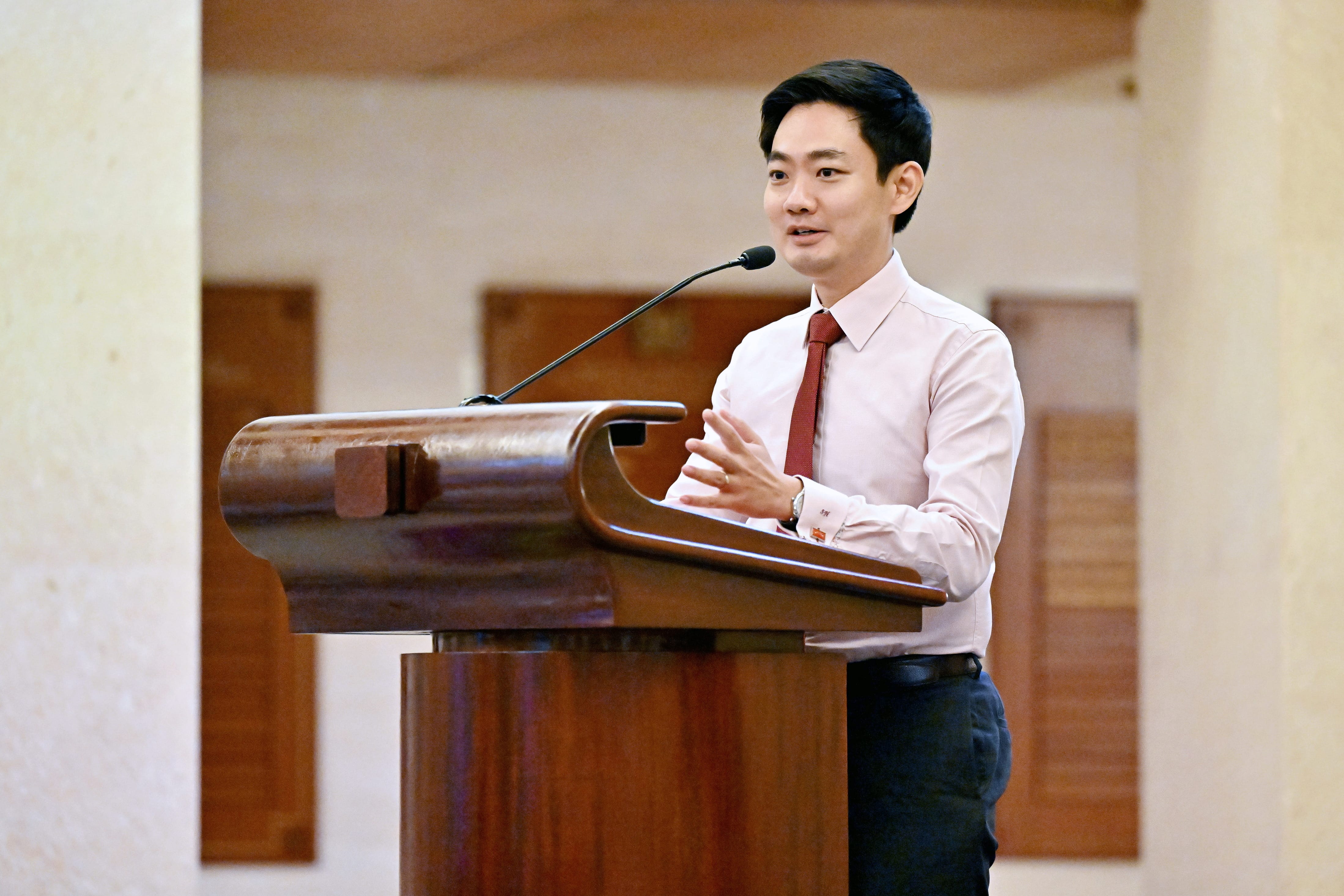 Speaker in white shirt and red tie addressing the audience at the podium