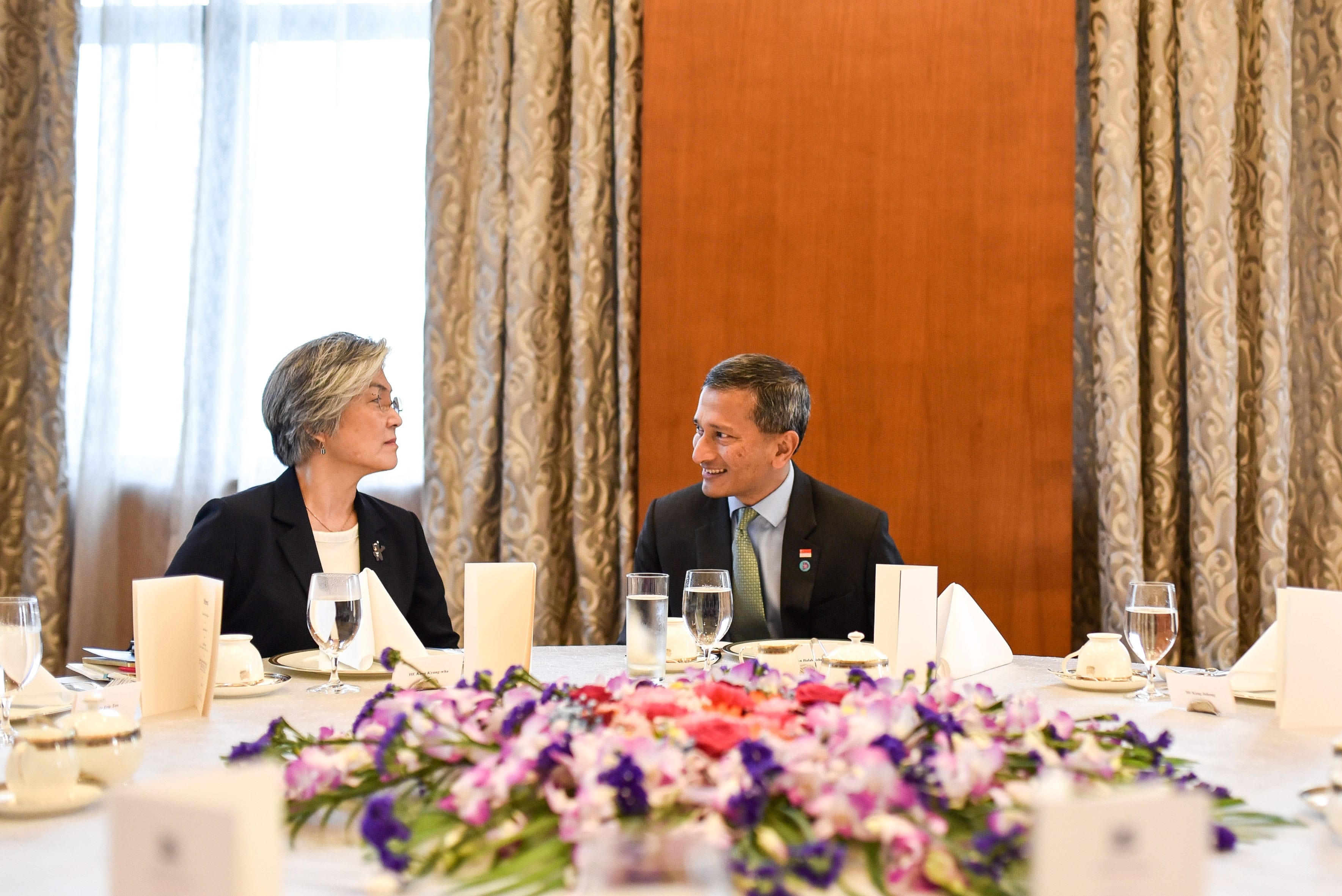 Woman and Vivian Balakrishnan sit at a formal table with flower centerpiece.