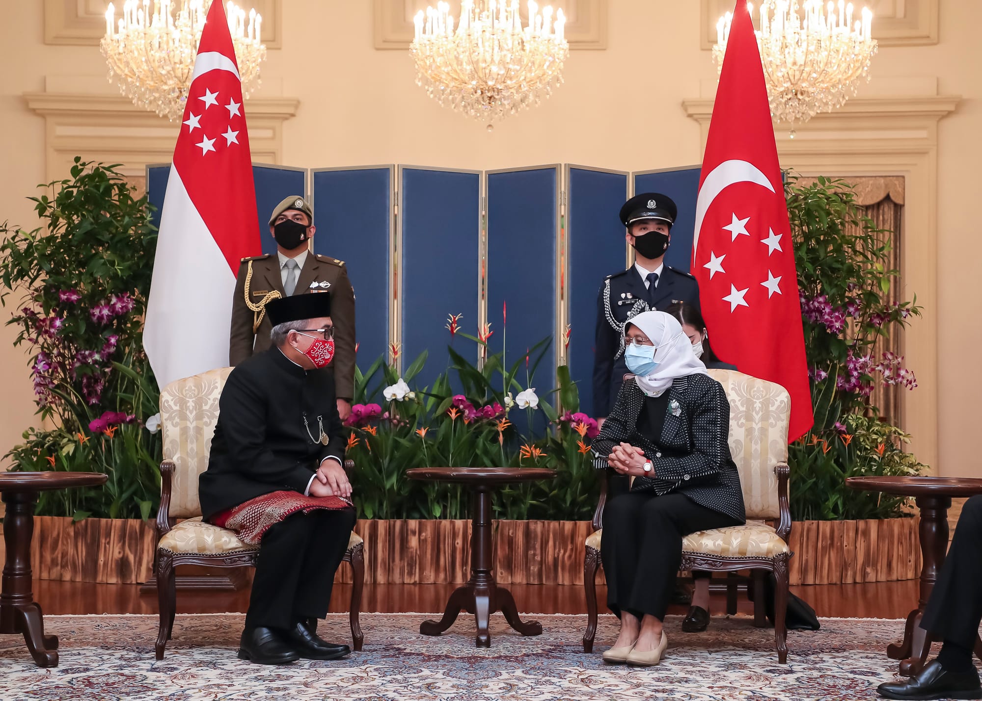 President Halimah Yacob meets with man. Singapore flags and uniformed staff in the background.
