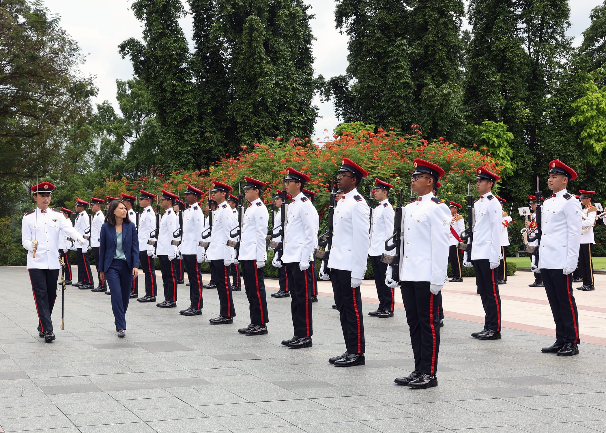 Parade of uniformed soldiers inspected by a woman in business attire.