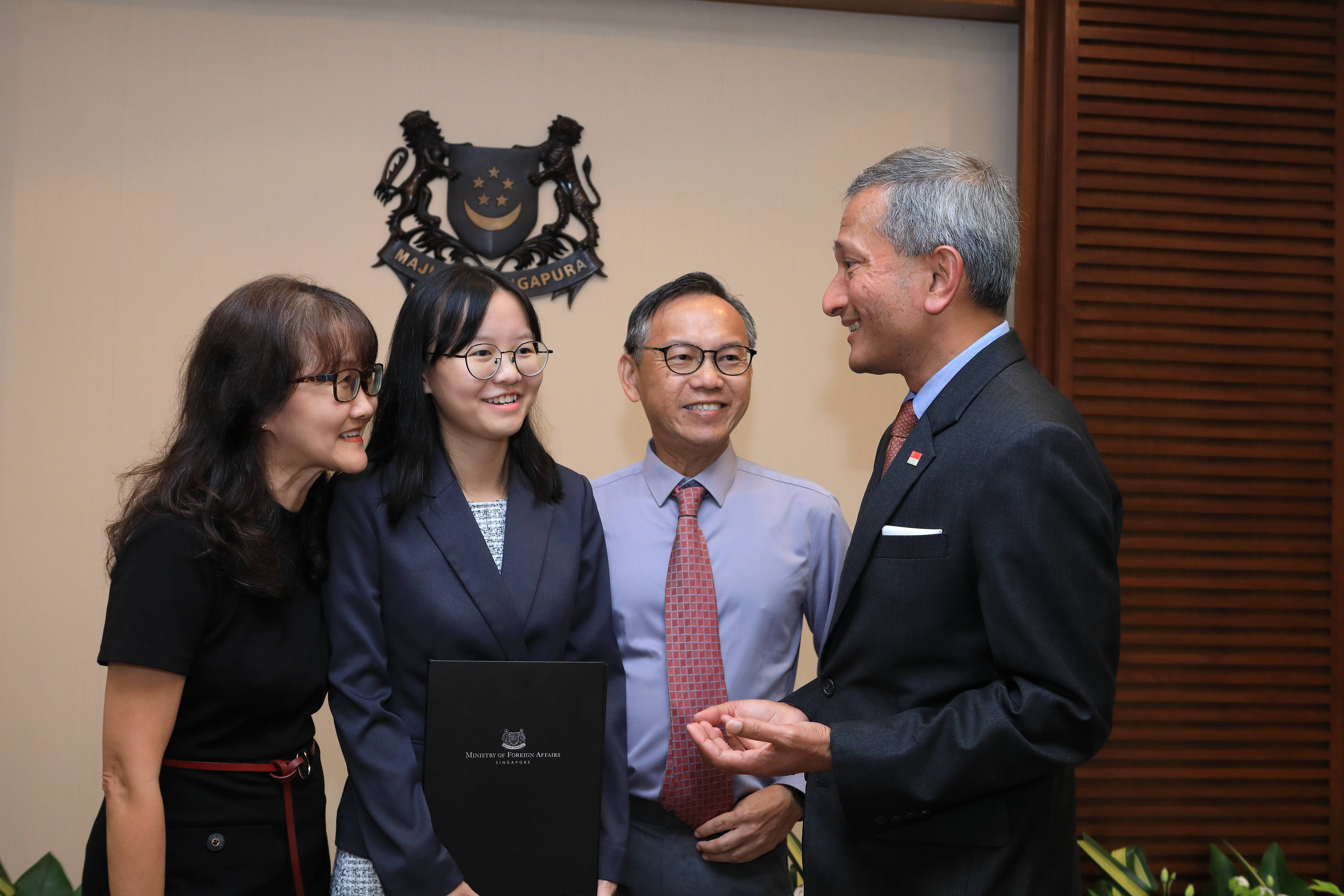 Group of people next to Singapore coat of arms, holding Ministry of Foreign Affairs folder.