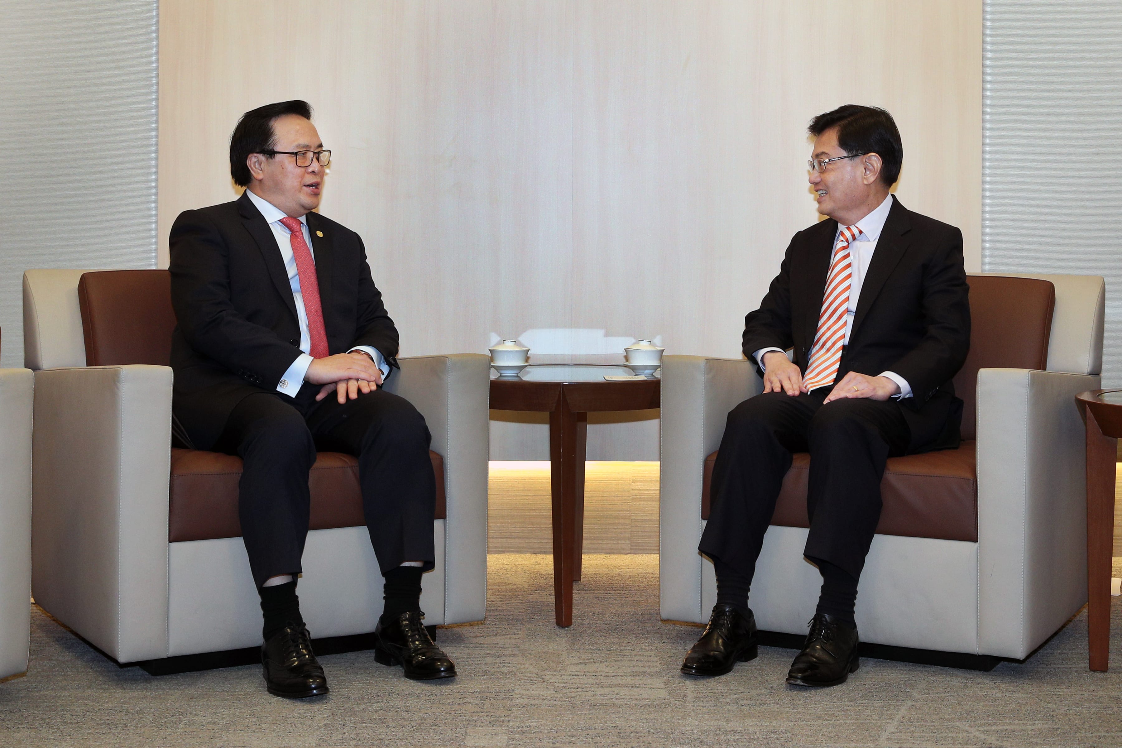 Two men in suits sitting in chairs facing each other in a meeting setting.