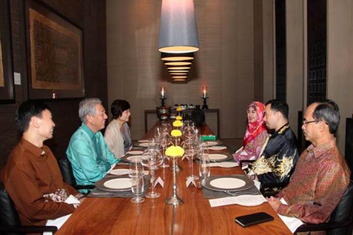 People seated at a long dining table set with plates, glasses, flowers, and candles.