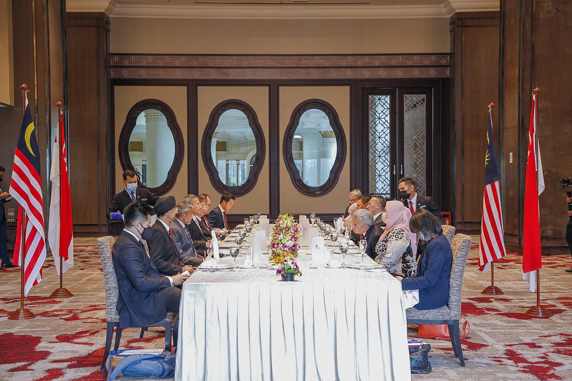 Group seated at a long table between Malaysian and Singaporean flags.