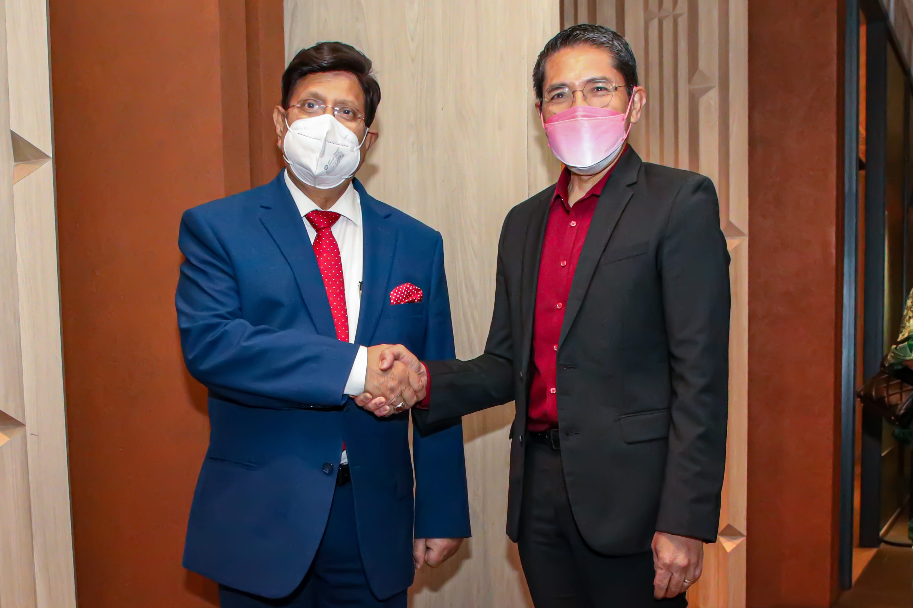 Two men in suits and face masks shaking hands indoors.