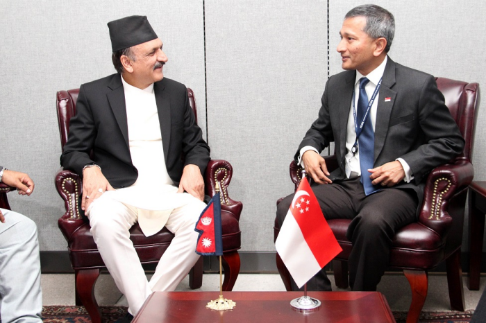 Two men in suits sit facing each other, with Nepal and Singapore flags on the table.