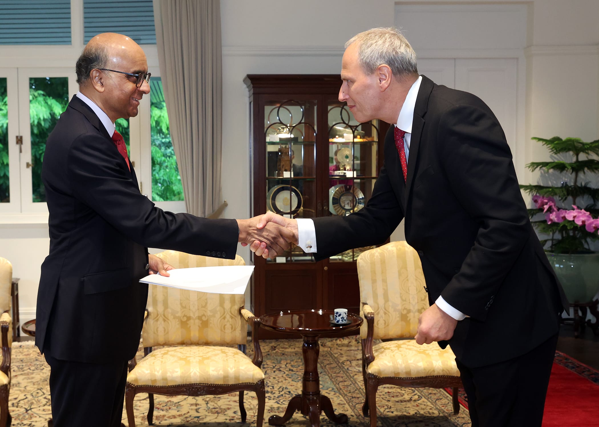 Two men in suits shaking hands, one holding papers.