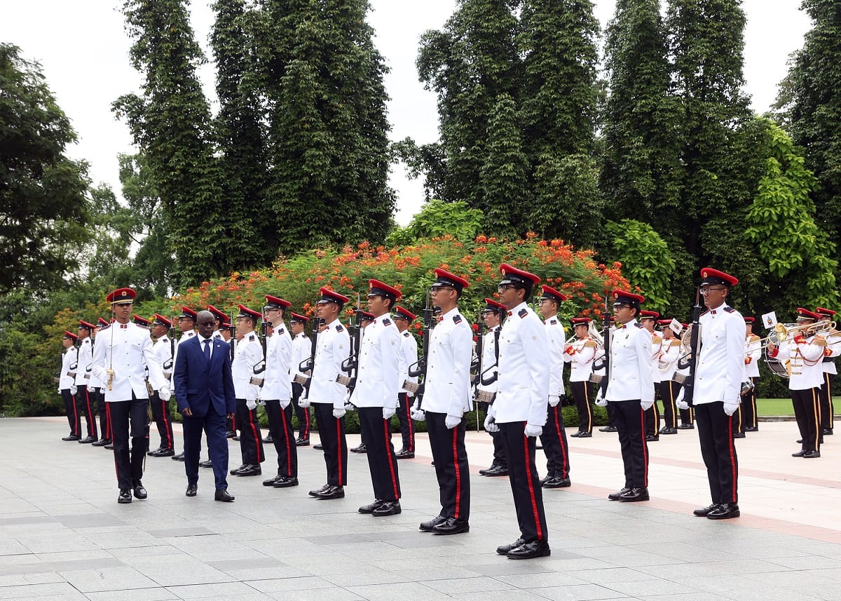 Two men walk past a military honor guard wearing red peaked hats and white uniforms.