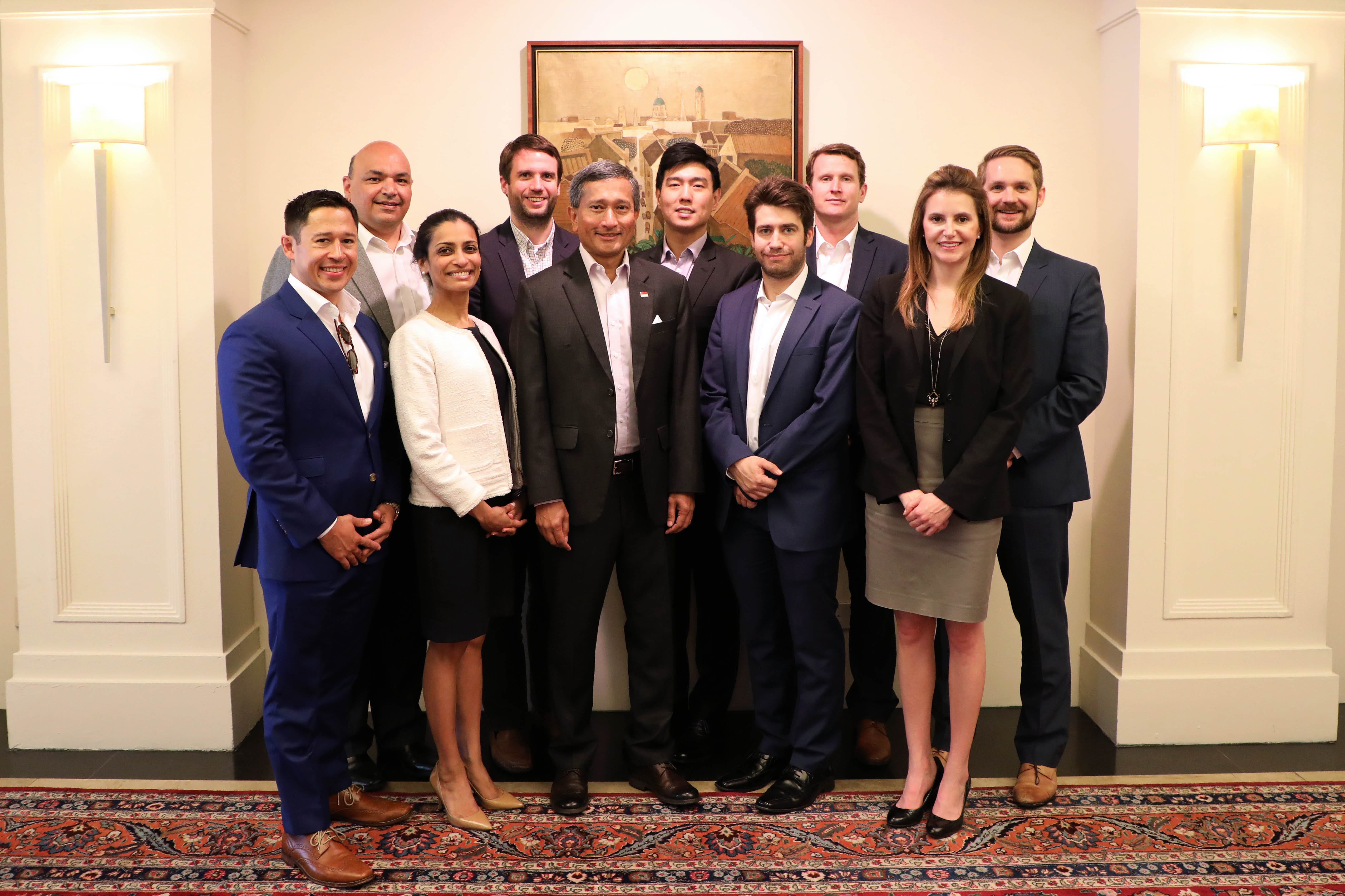 Group of ten people in business attire posing indoors near a painting.