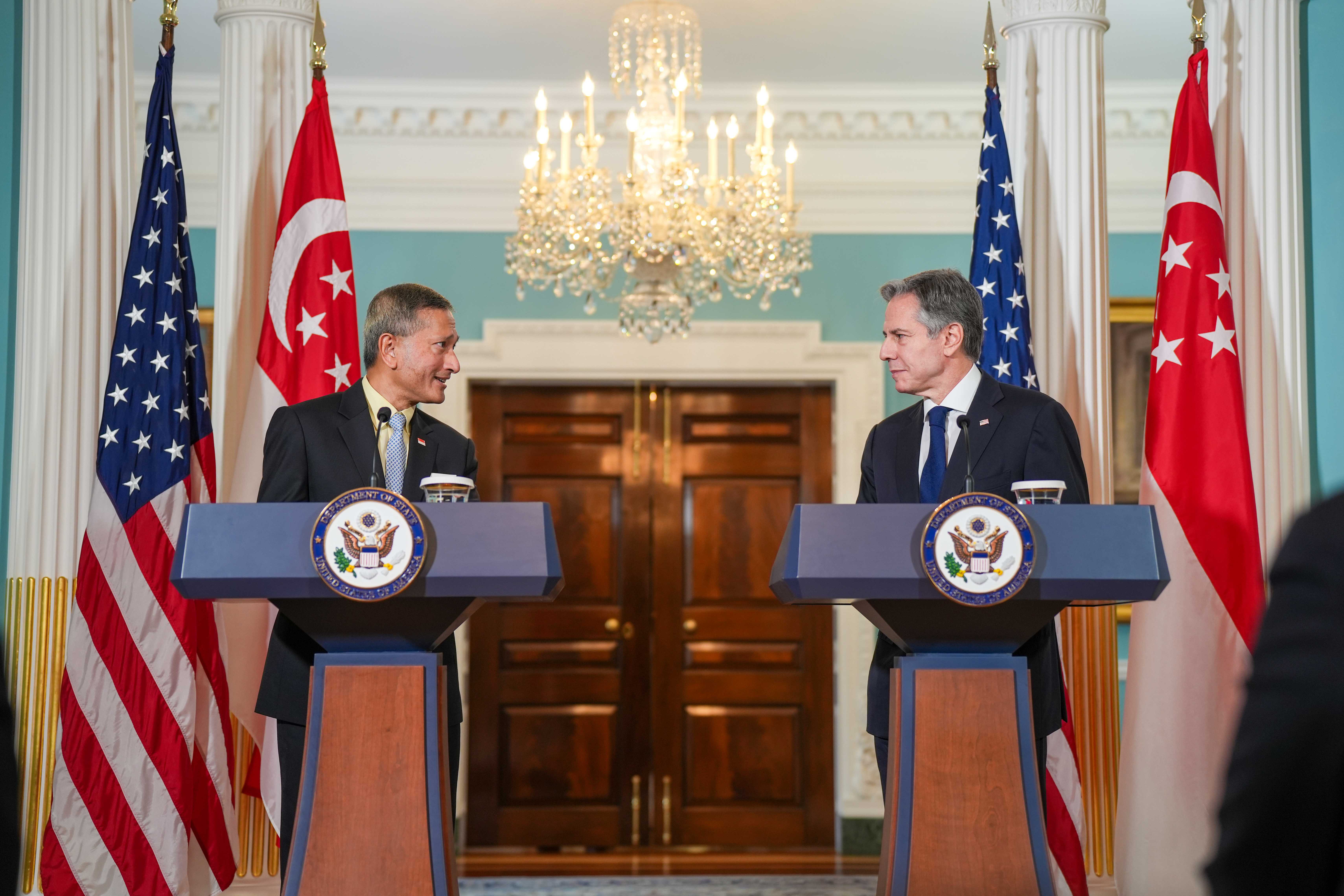 Blinken and Singaporean official stand at podiums with US and Singapore flags.