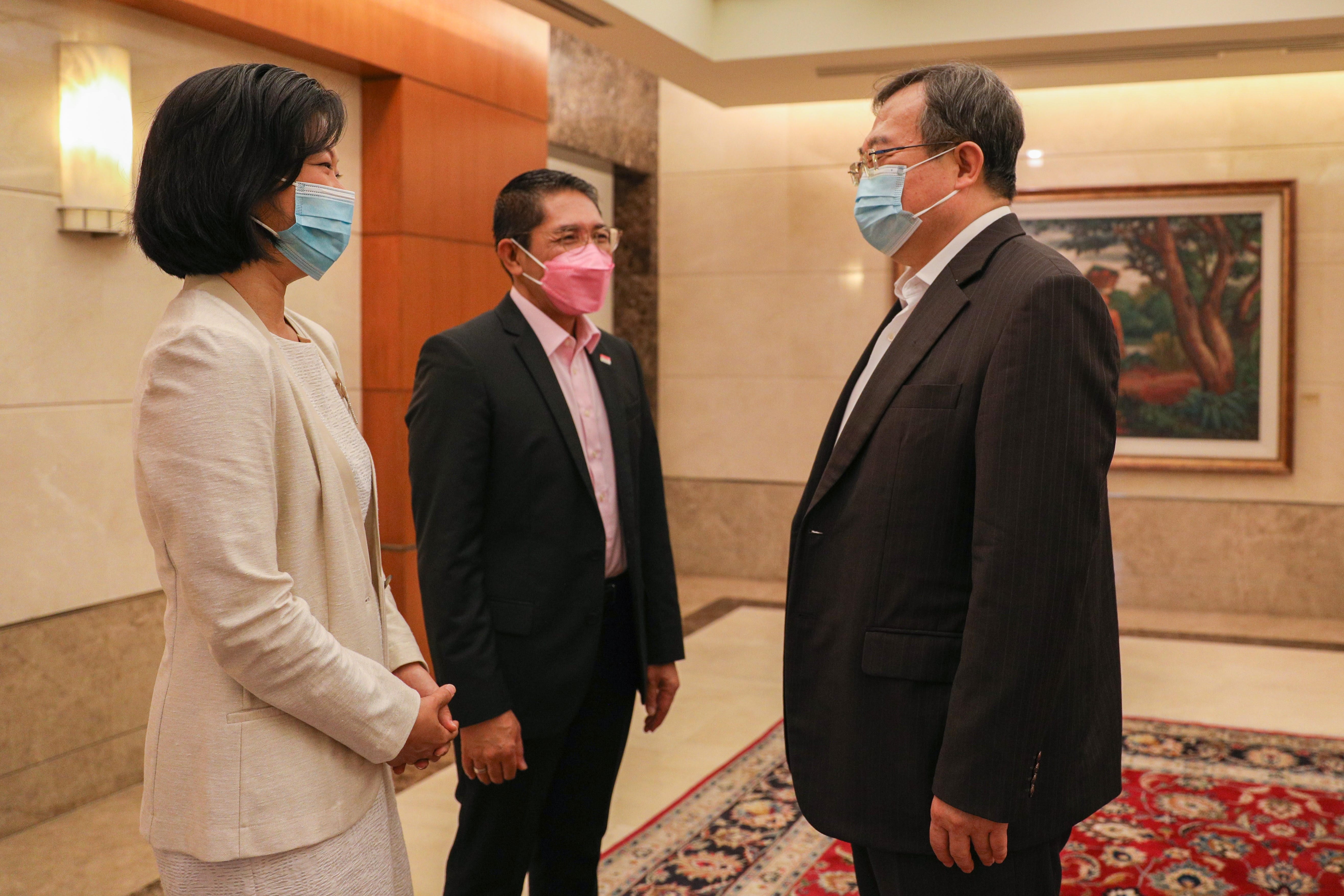 Three people in suits wearing face masks stand in a decorated room.