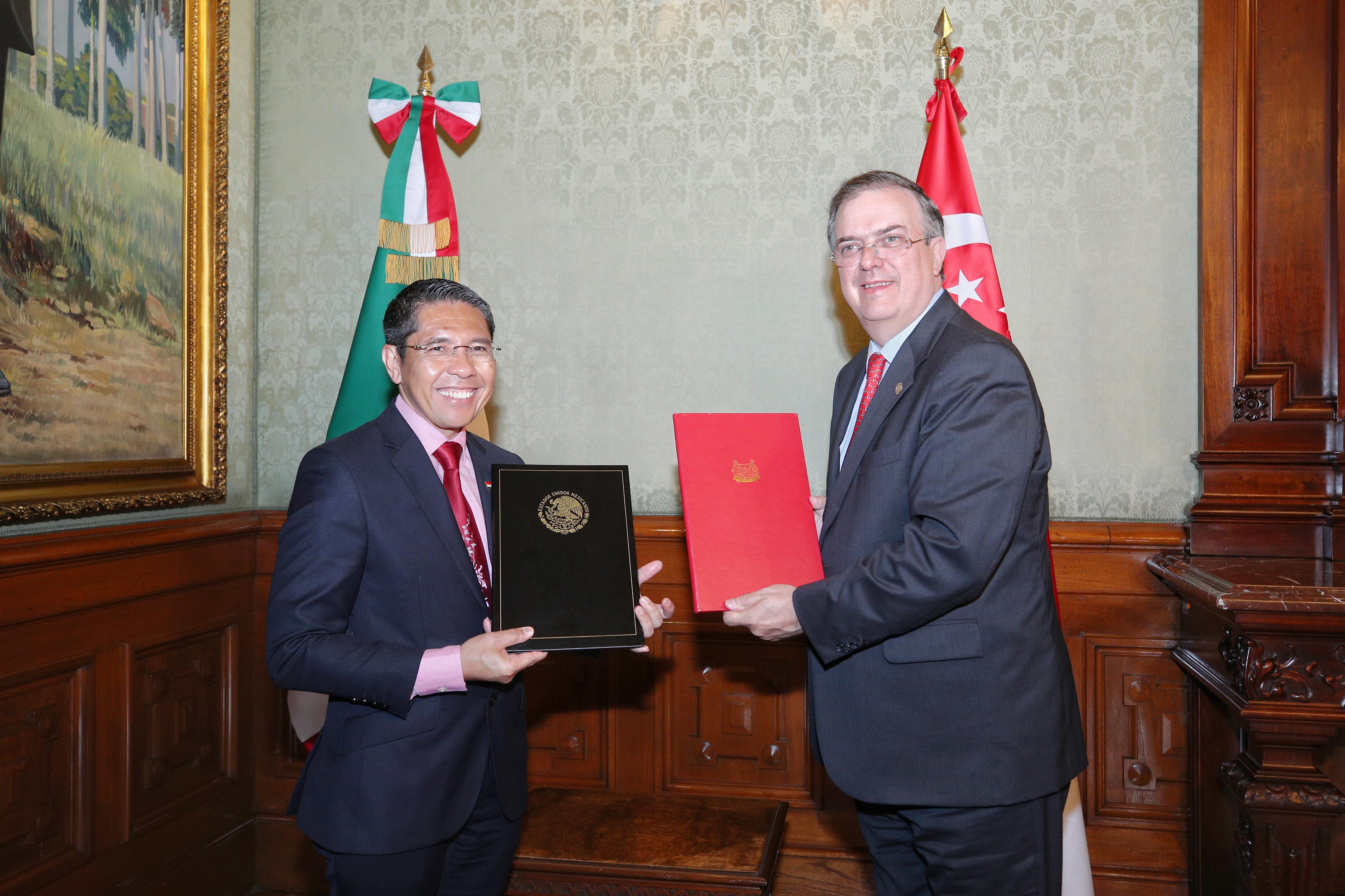 Three men in suits pose before flags and a "Global Coalition to Defeat ISIS" sign. One wears traditional Arab dress.