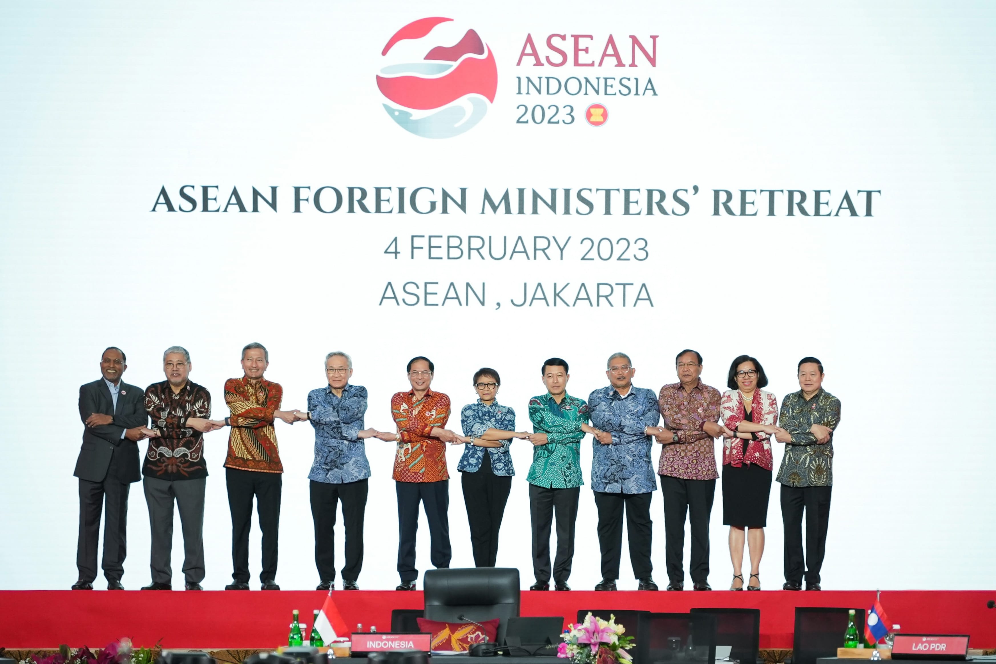 Ten people holding hands on a red stage below "ASEAN FOREIGN MINISTERS' RETREAT".