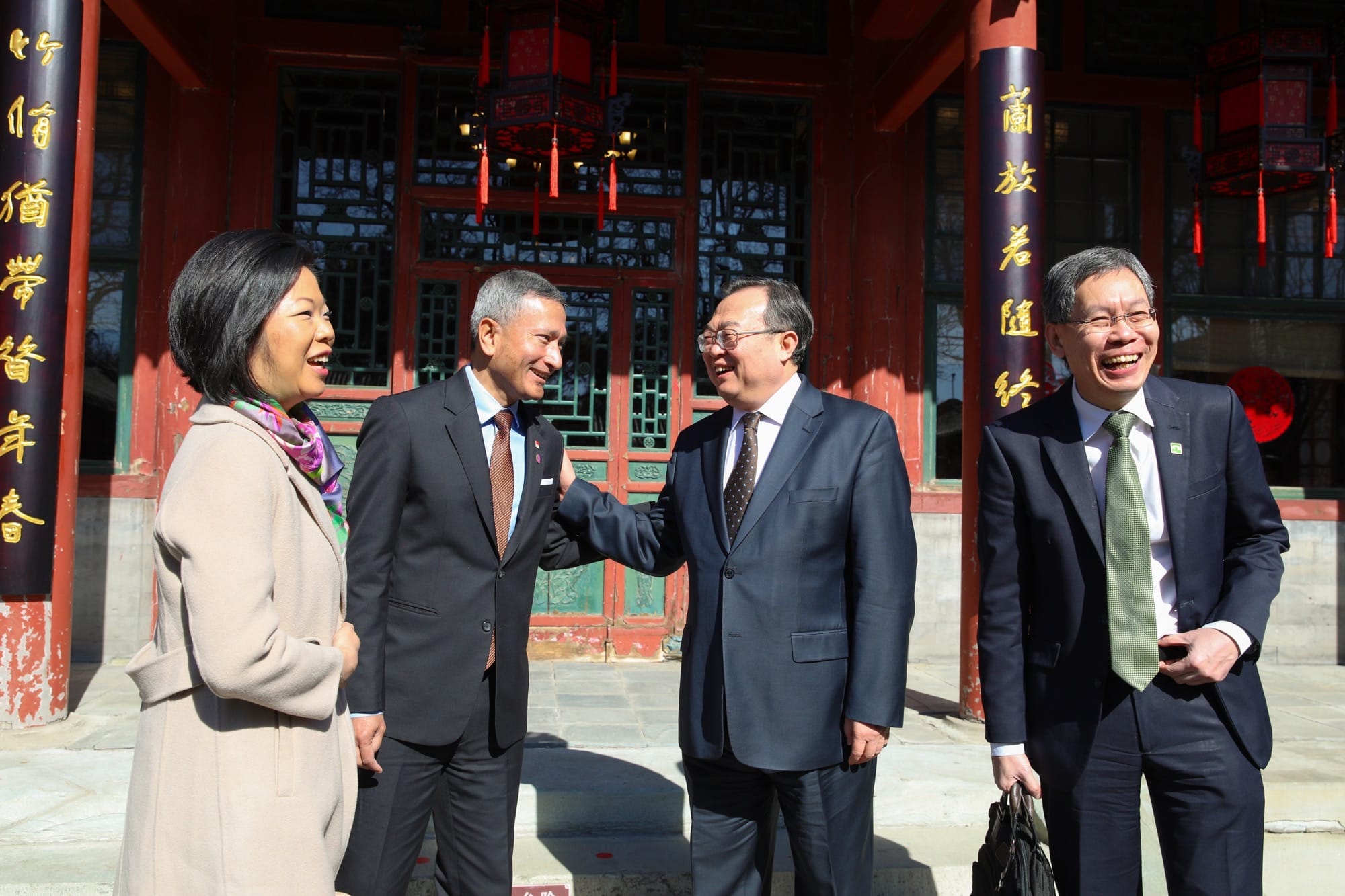 Four people in suits stand outside a red building with Chinese characters.