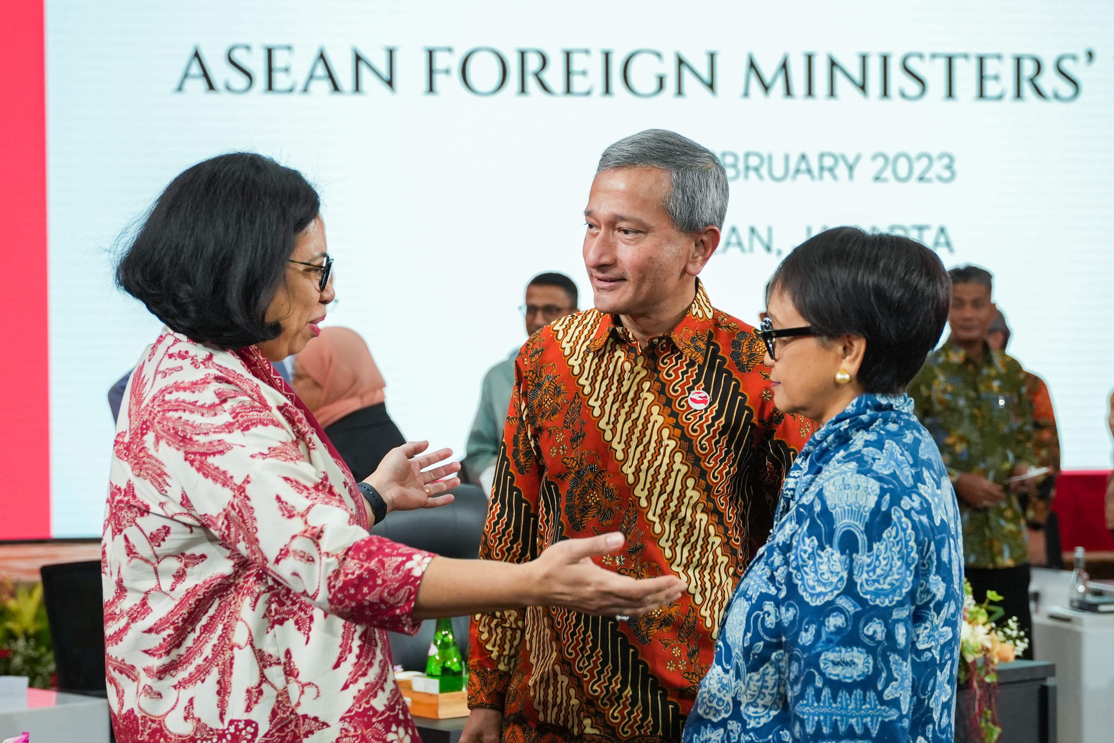 Three people in patterned shirts converse in front of an "ASEAN FOREIGN MINISTERS'" backdrop.