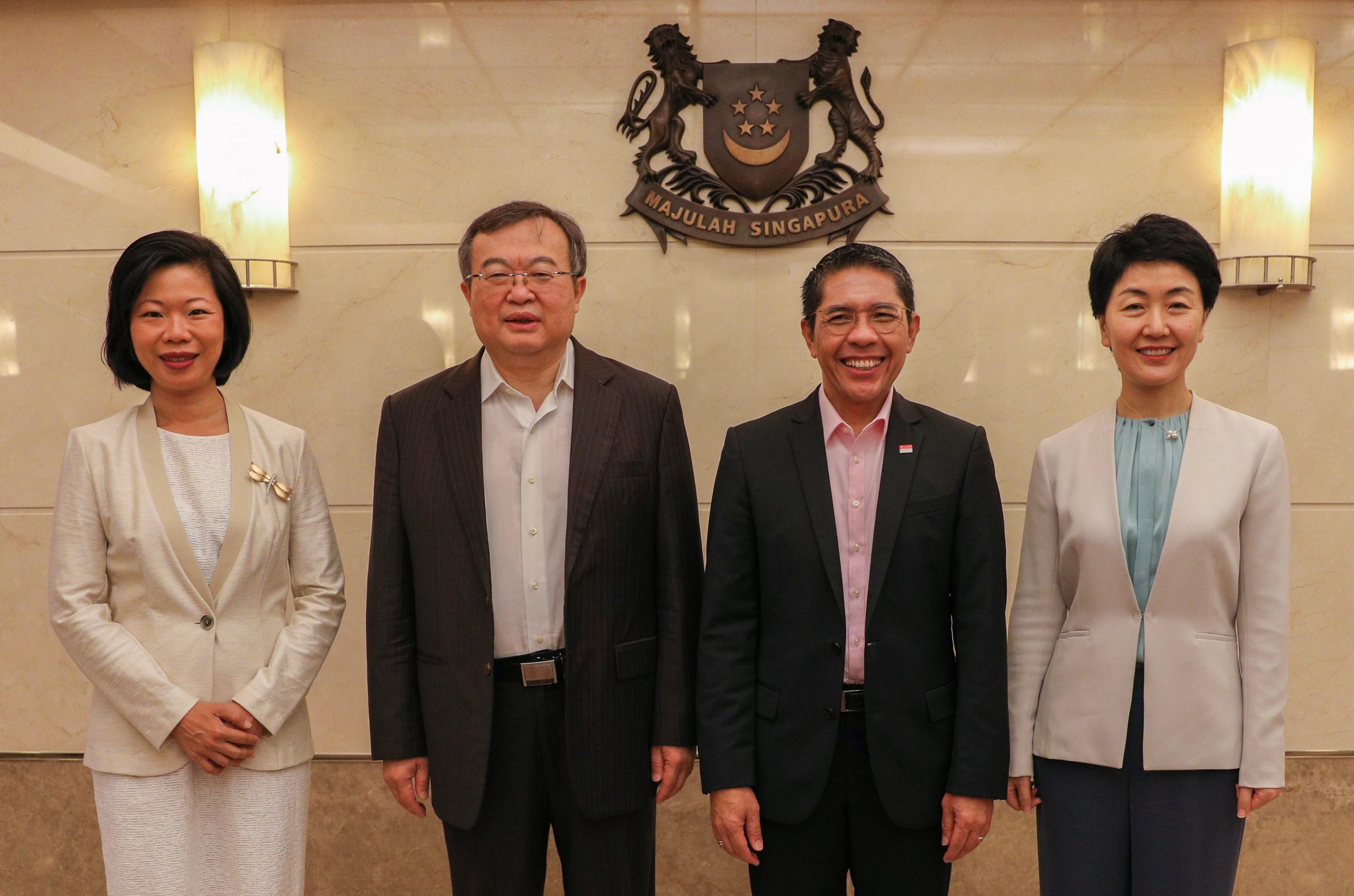 Four people in formal attire stand before the Majulah Singapura emblem.