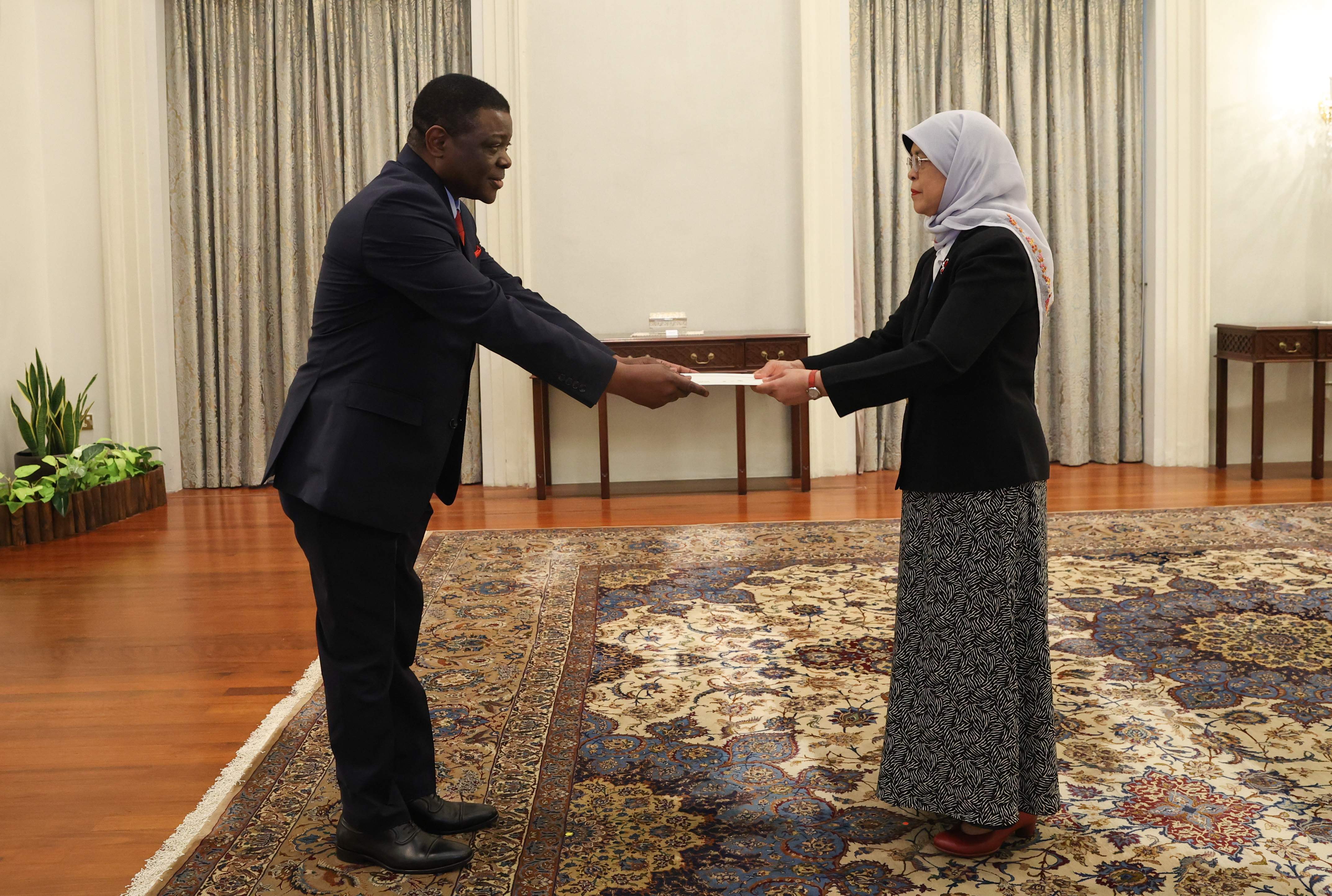 Two people in suits exchanging a document in ornate room.