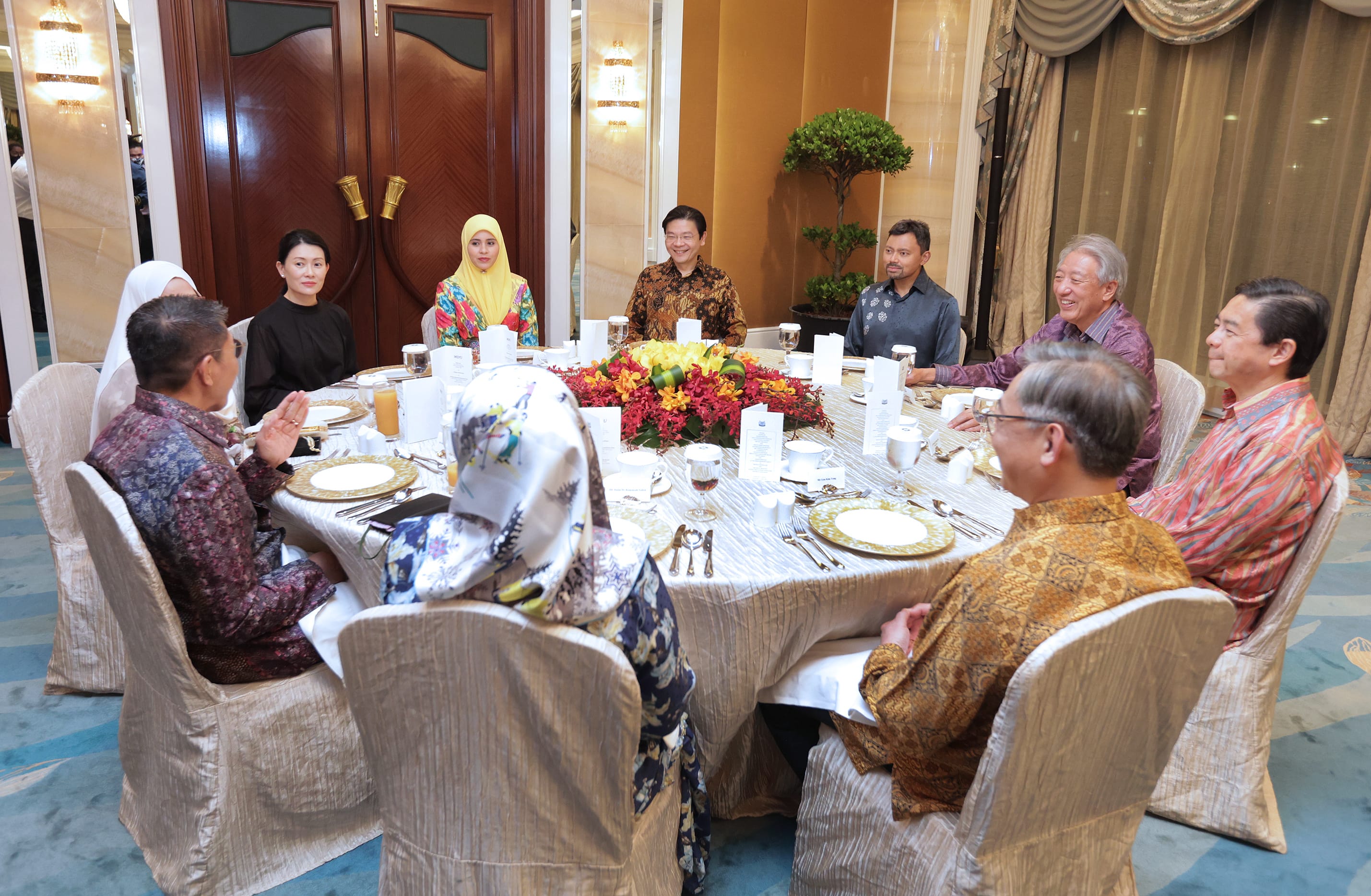 Group of people seated around a table set for a meal in a formal setting.