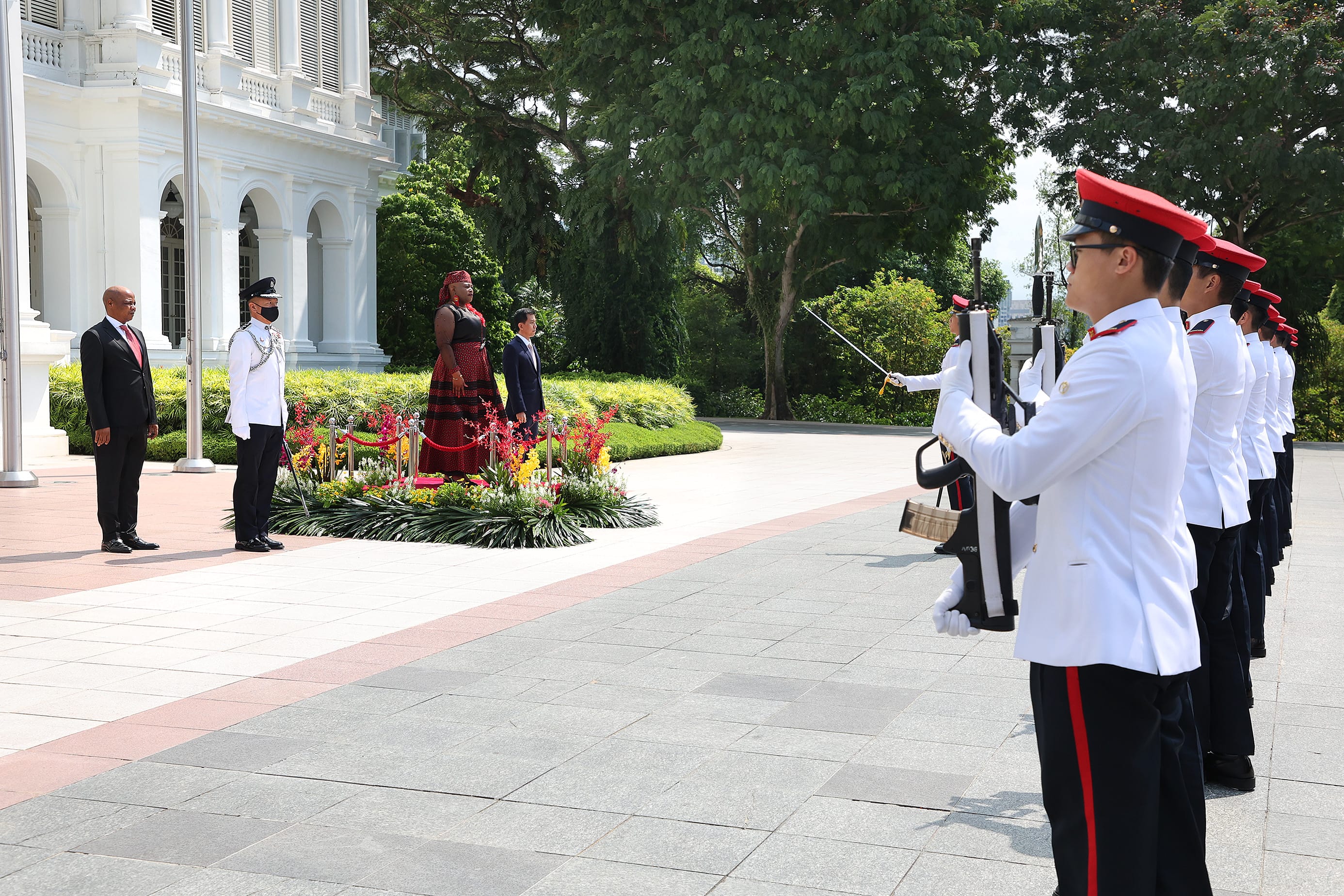 Formal visit with honor guard holding rifles and swords in front of white building.