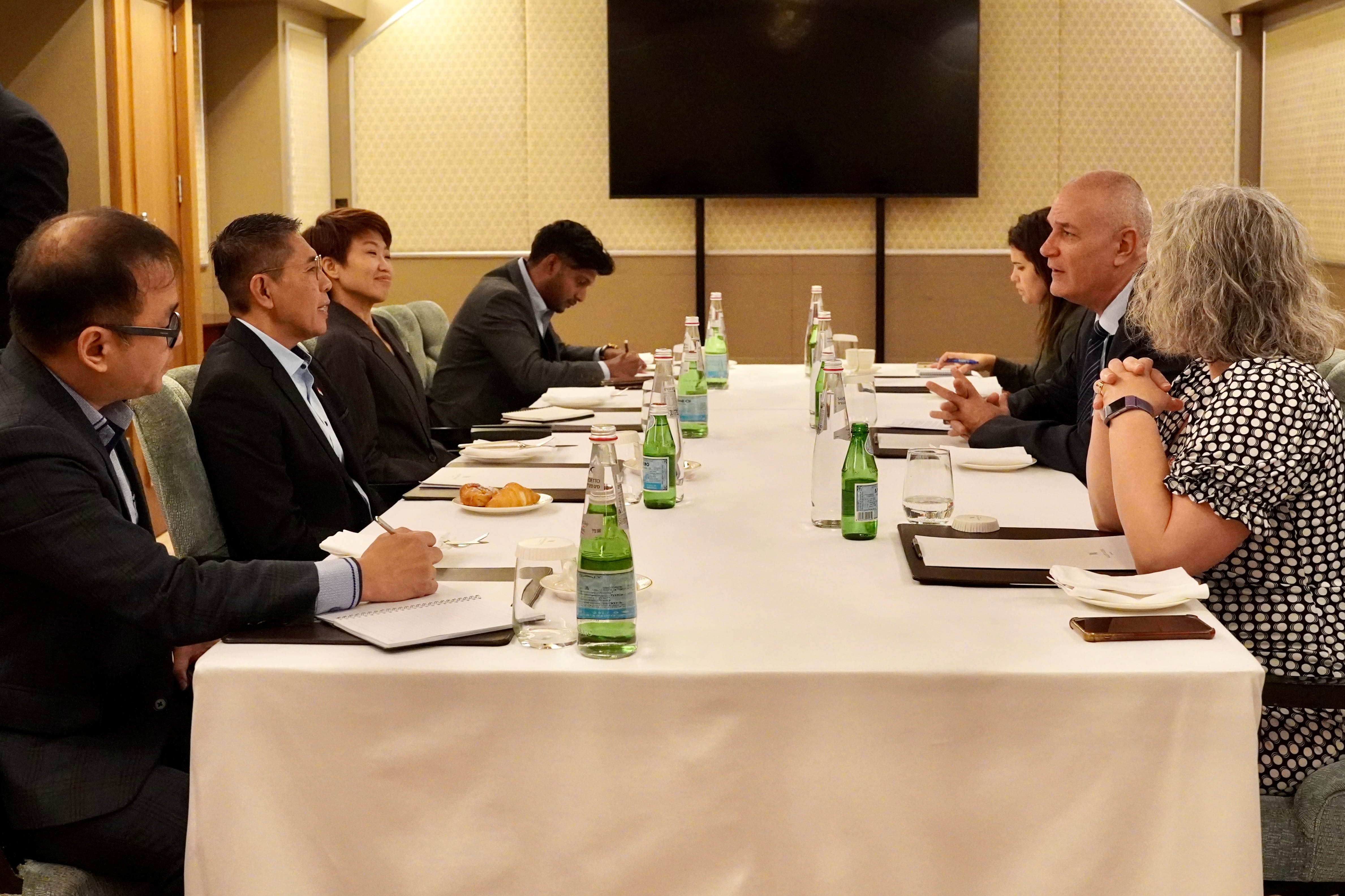 People seated at a long table with water bottles and writing pads in a meeting setting.