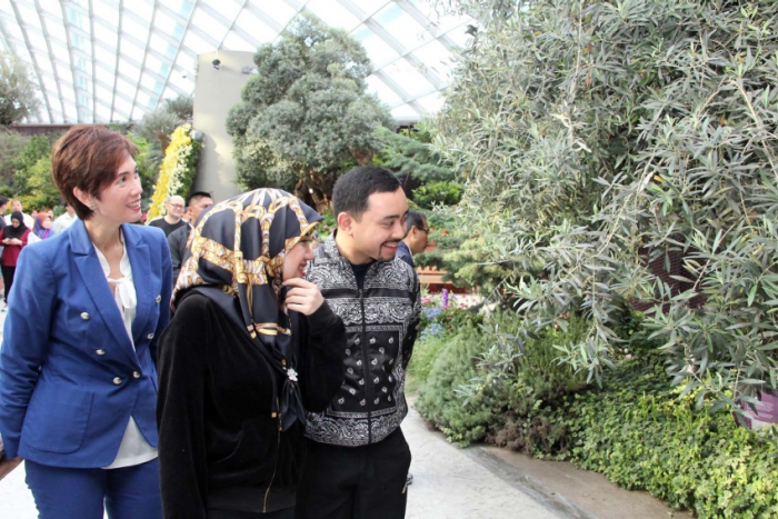 Three people walk among lush foliage in an indoor garden setting.
