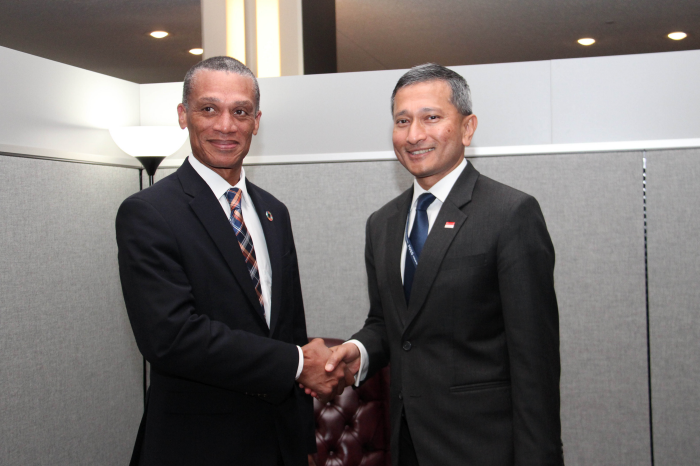 Two men in suits shake hands, one with Indonesian flag pin.