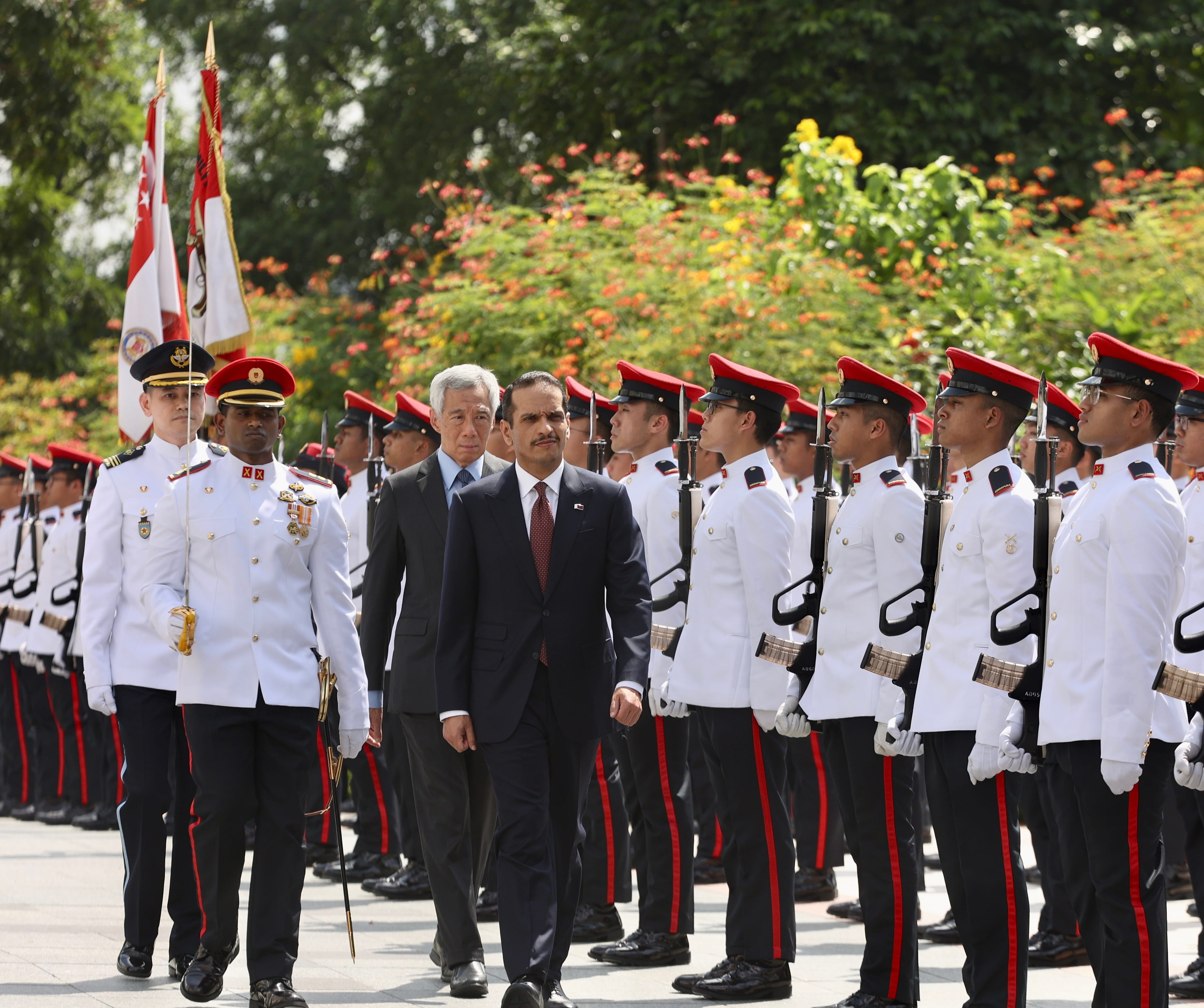 Justin Trudeau and Lee Hsien Loong shaking hands indoors, formal wear, flowers, glass doors.