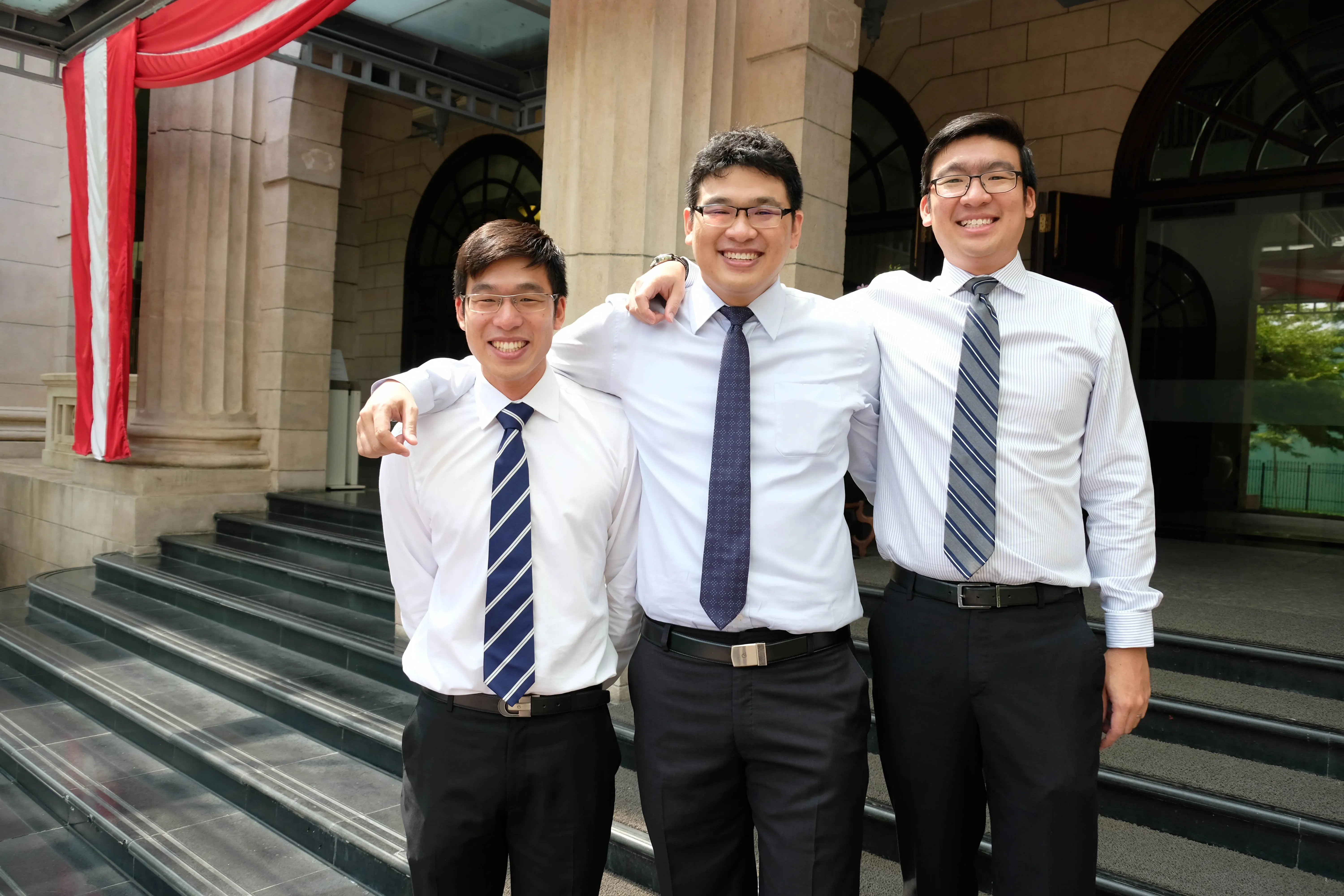 Three men in business attire posing together outside a modern building.