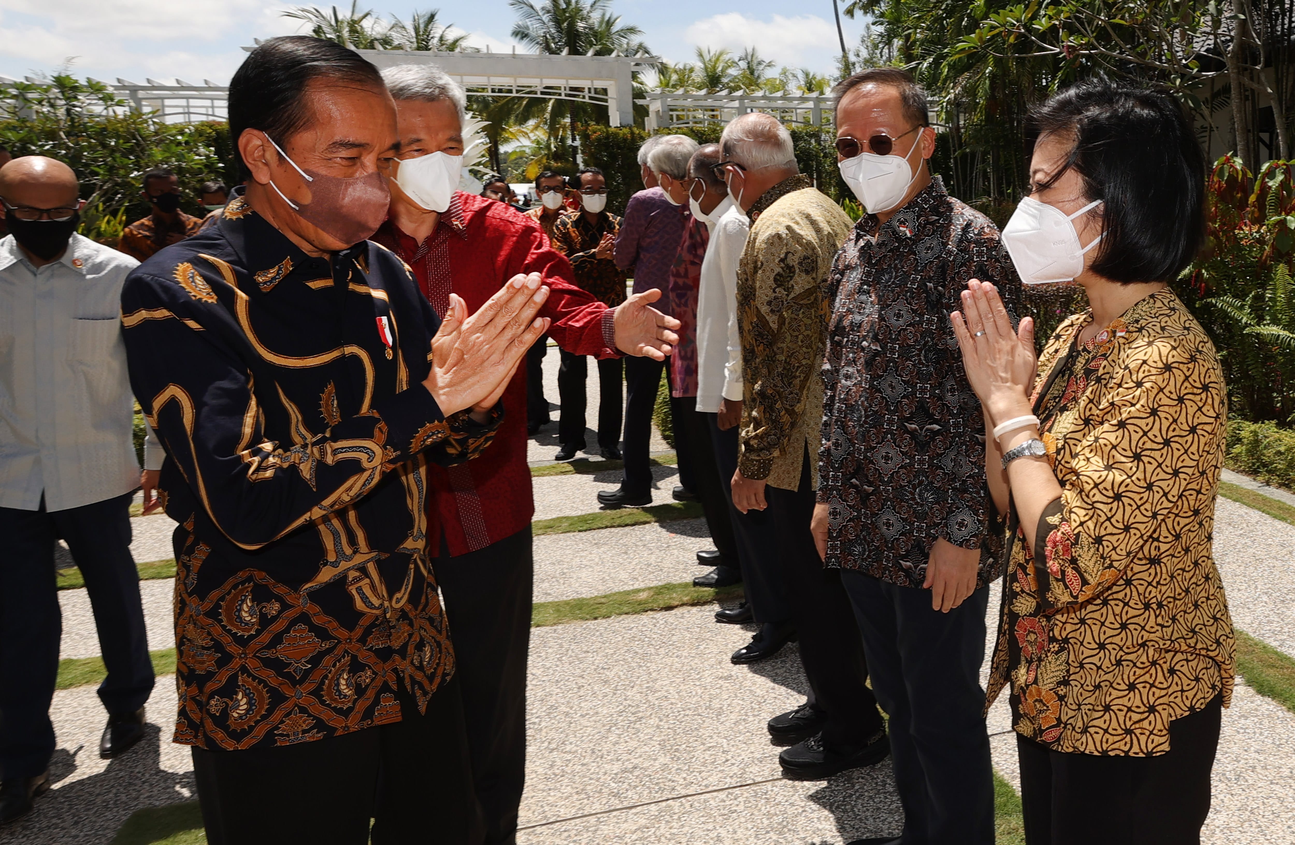 Line of people in batik clothing, wearing face masks, hands clasped in greeting.