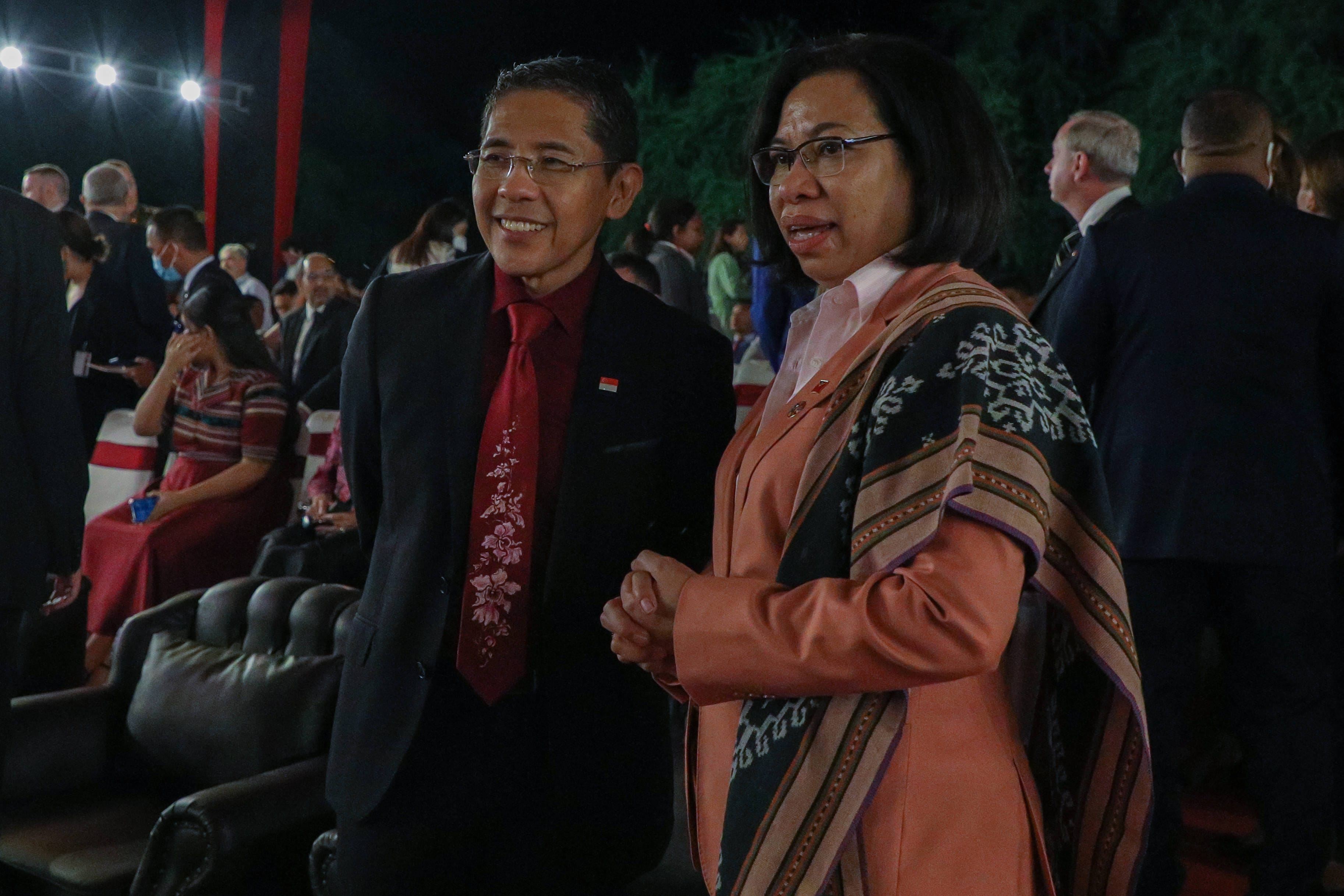 Two people in business attire stand in a crowd. One wears a red tie with an Indonesian flag pin.
