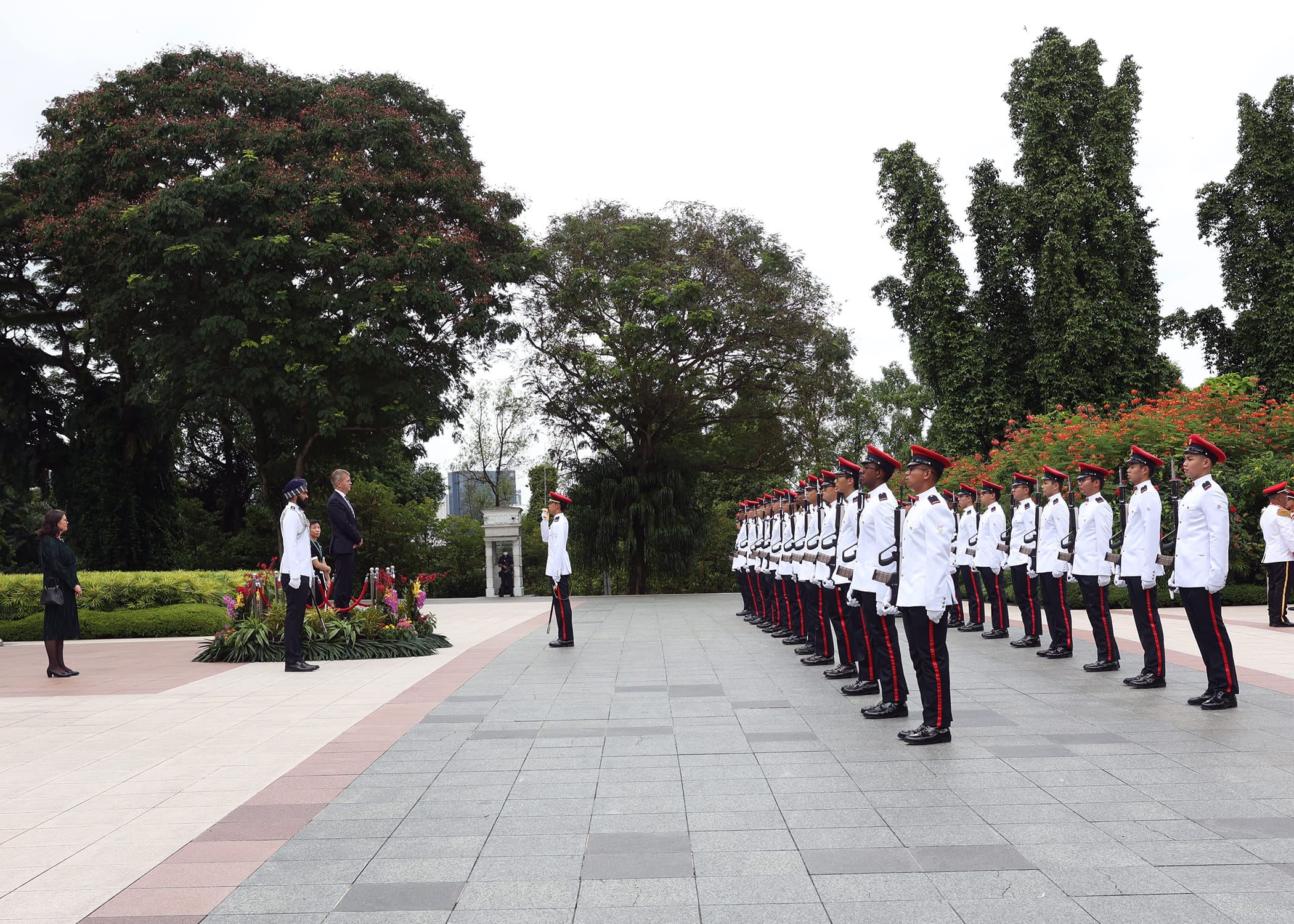 Honor guard in white and red uniforms stand at attention on a stone plaza.