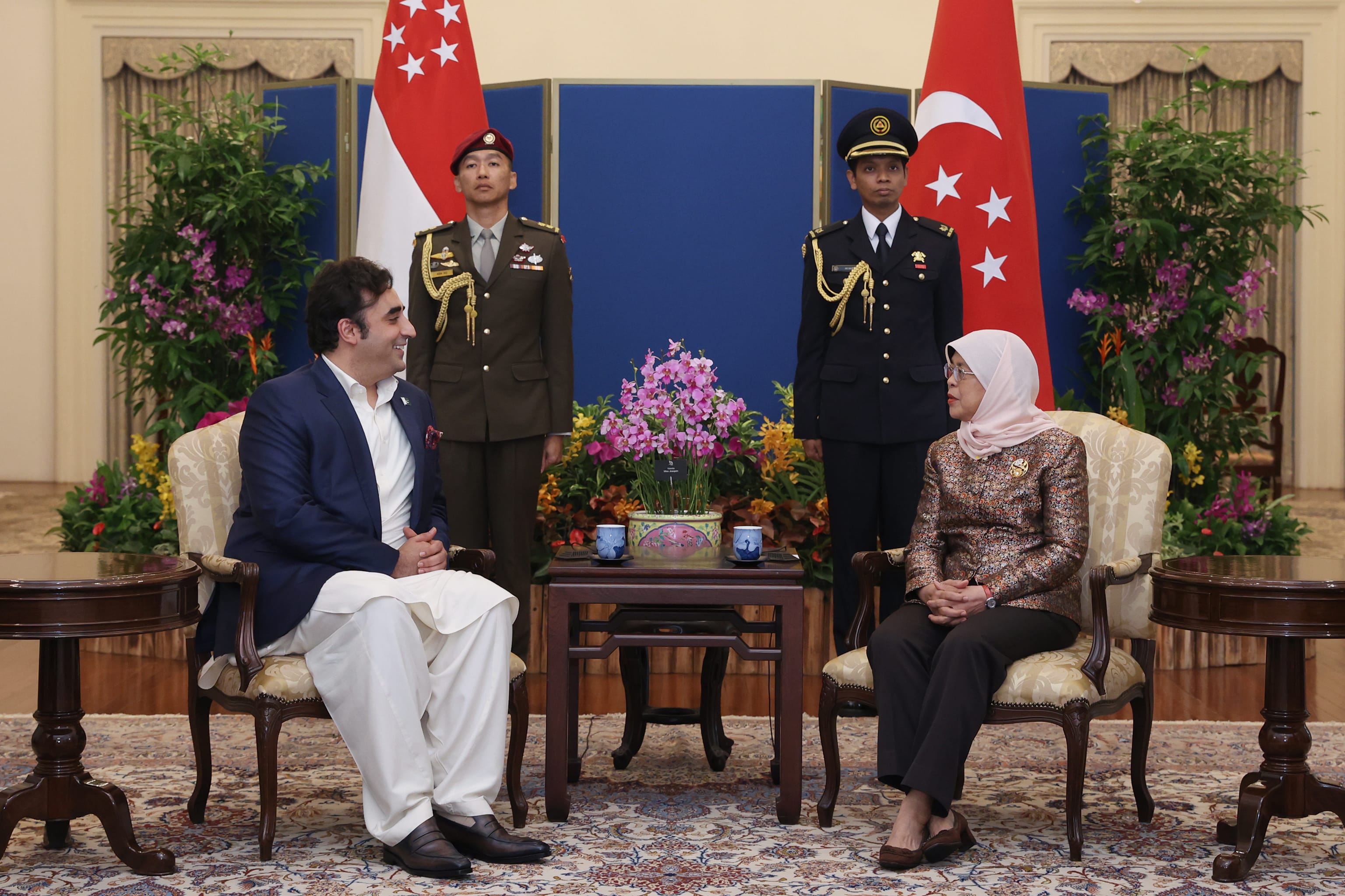 Man and Halimah Yacob sit, flanked by soldiers and Singapore flags.