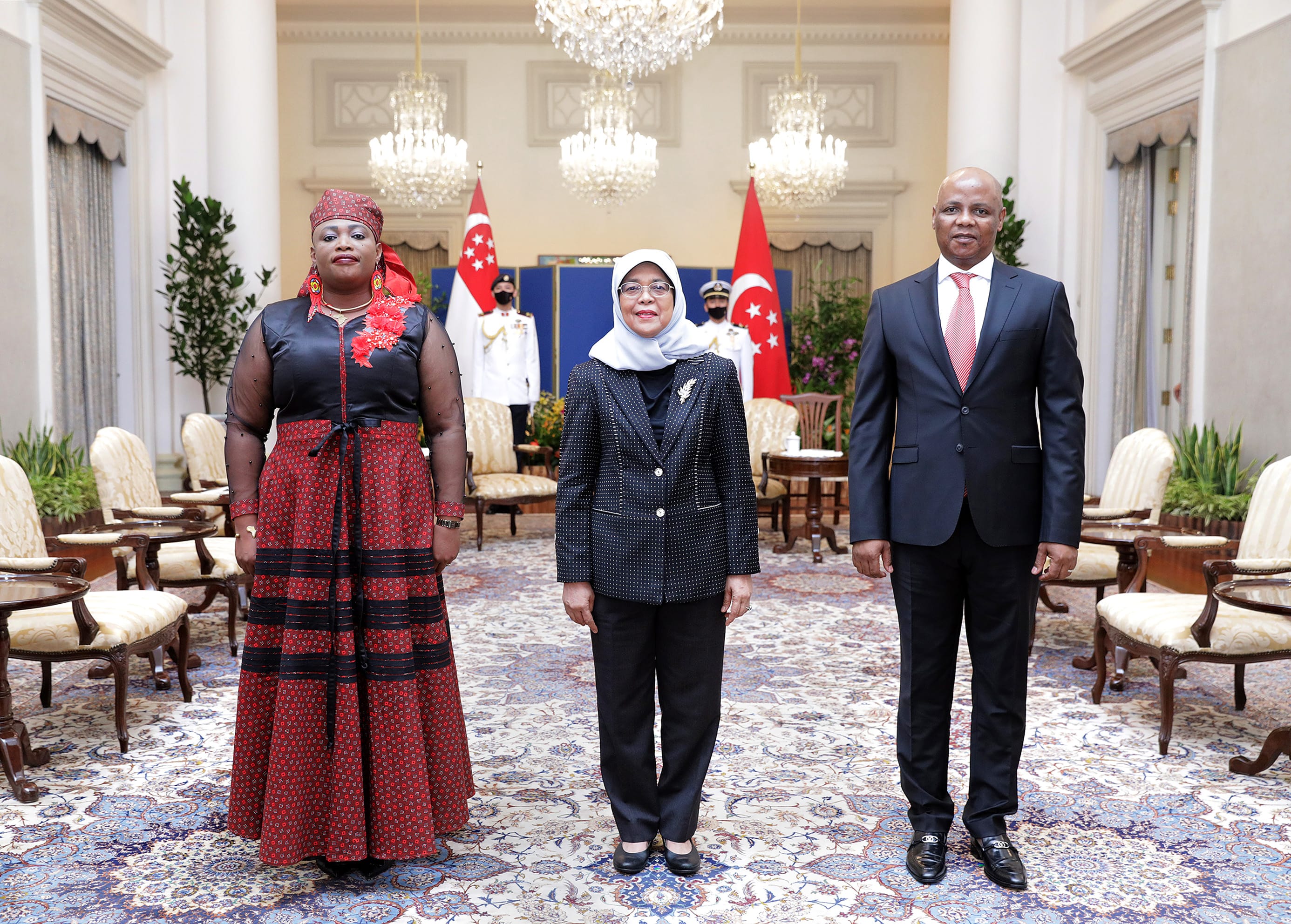 Three people stand in a room with Singaporean and Turkish flags.