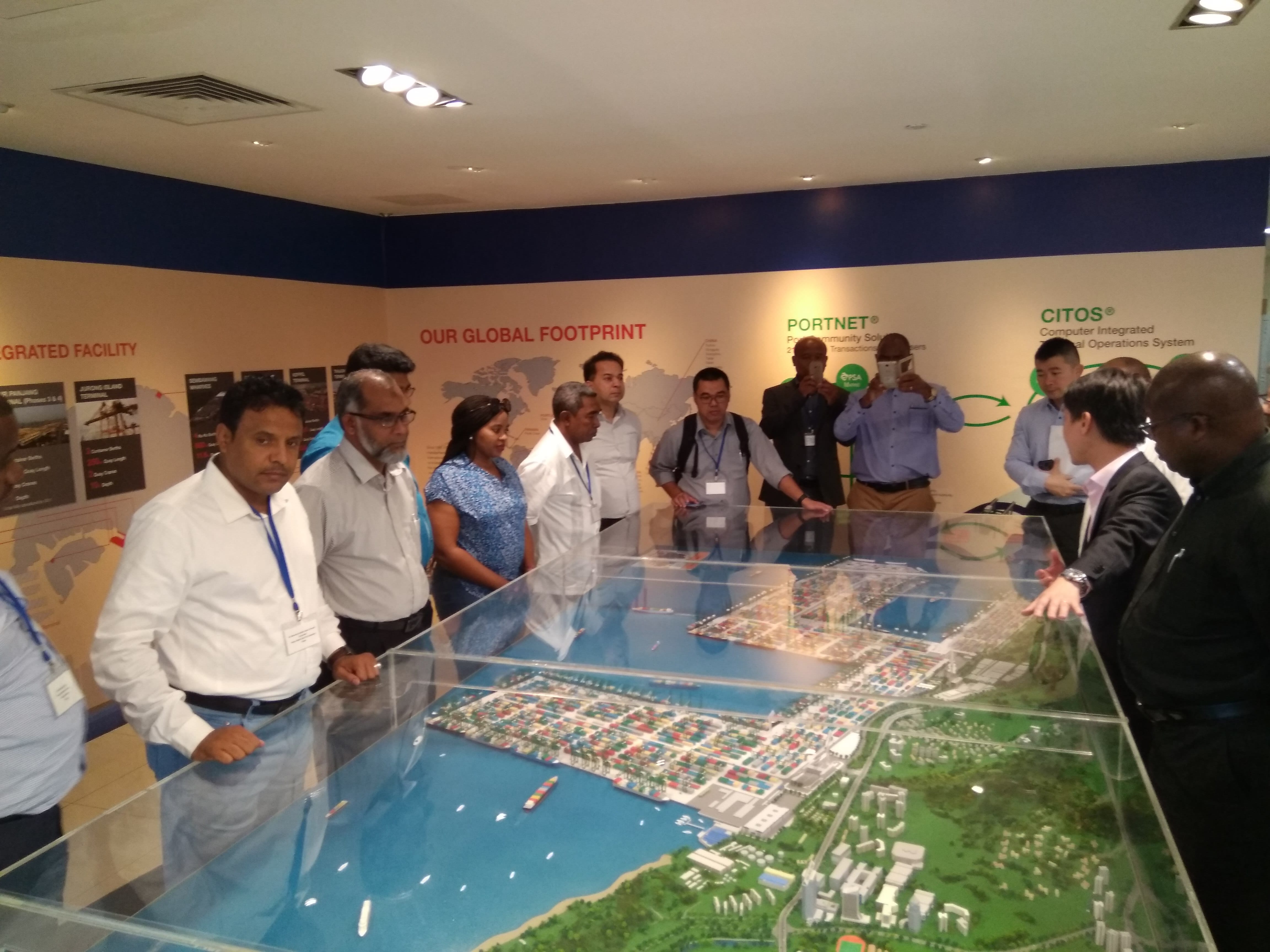 Group looking at a city model with water, container port, and greenery under glass.
