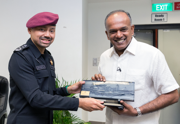 Man in uniform presents bas-relief image of building to smiling man in white shirt.