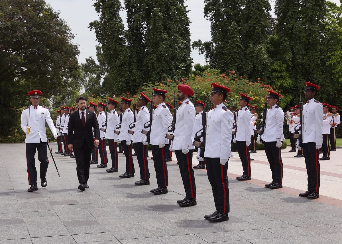 Volodymyr Zelenskyy inspects honor guard in white uniforms with red hats.