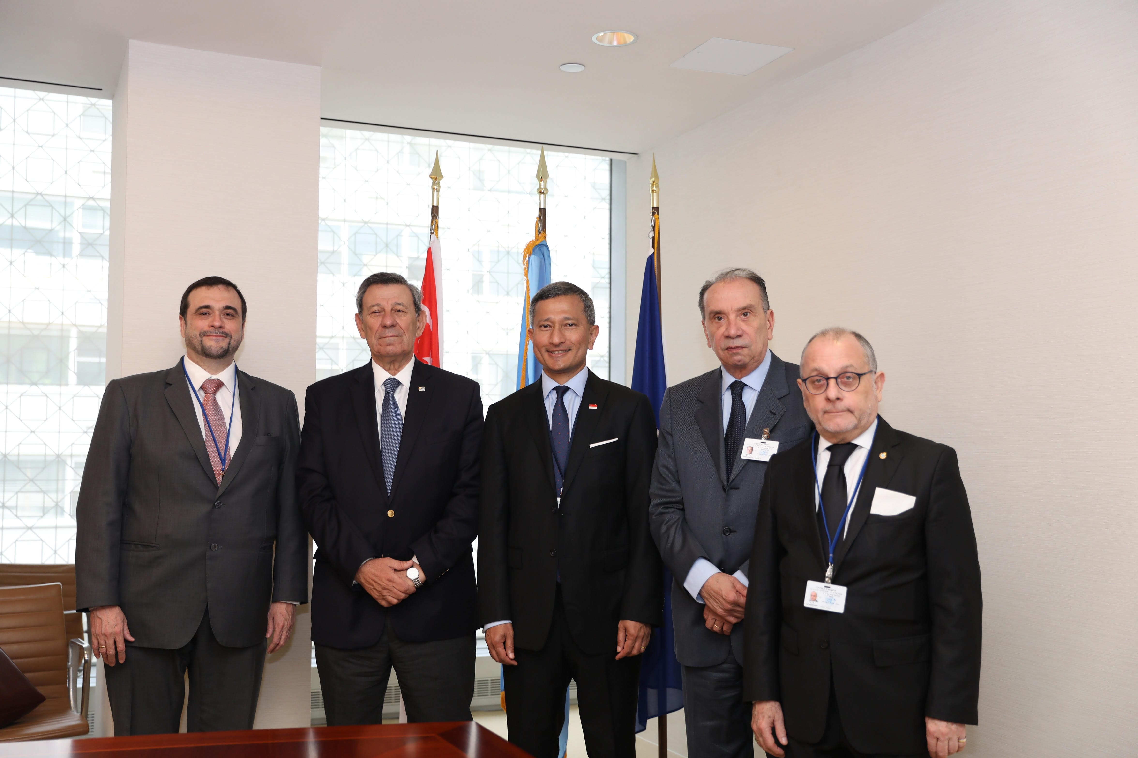 Five men in suits stand before flags.