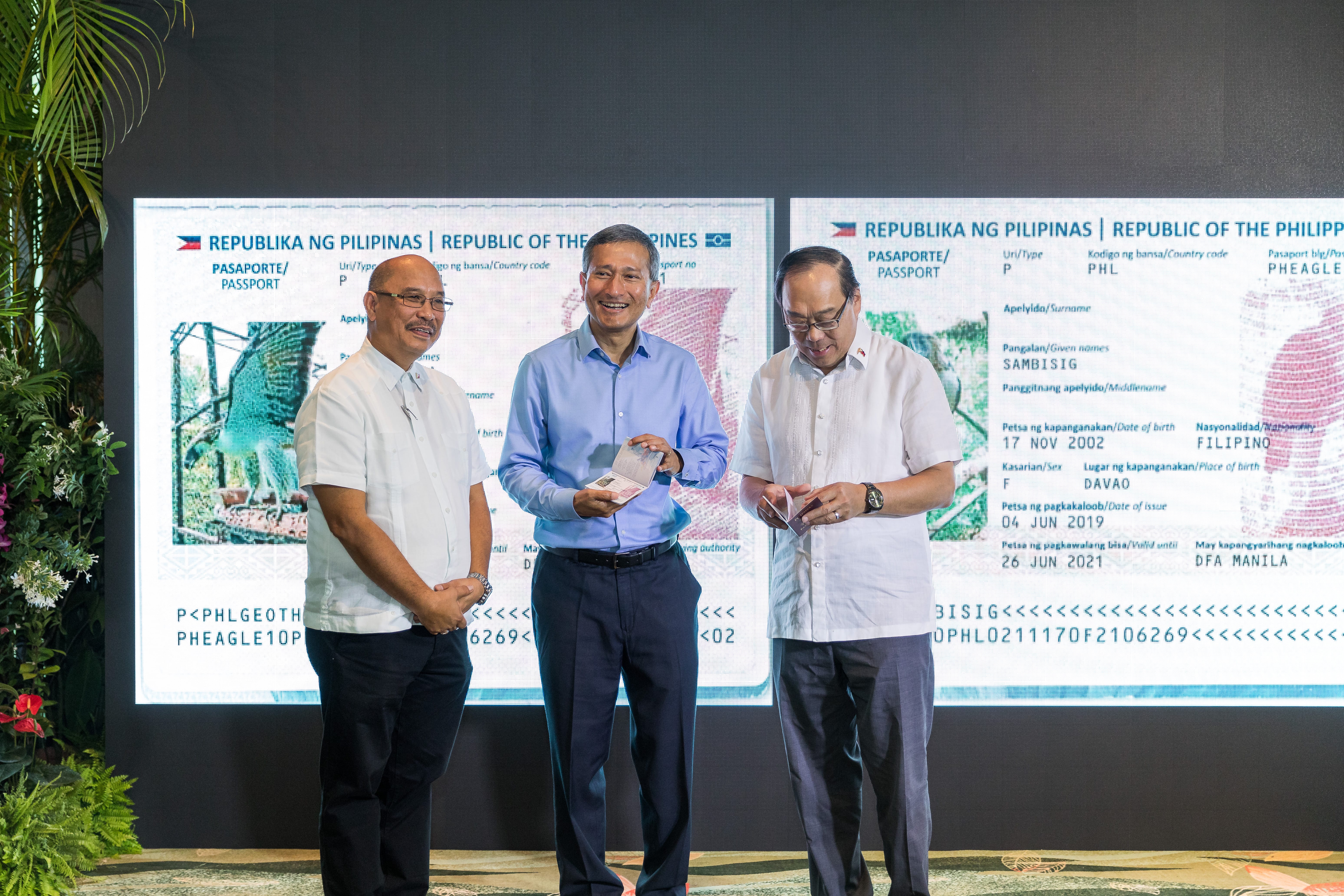 Three men stand before a display of Filipino passports.