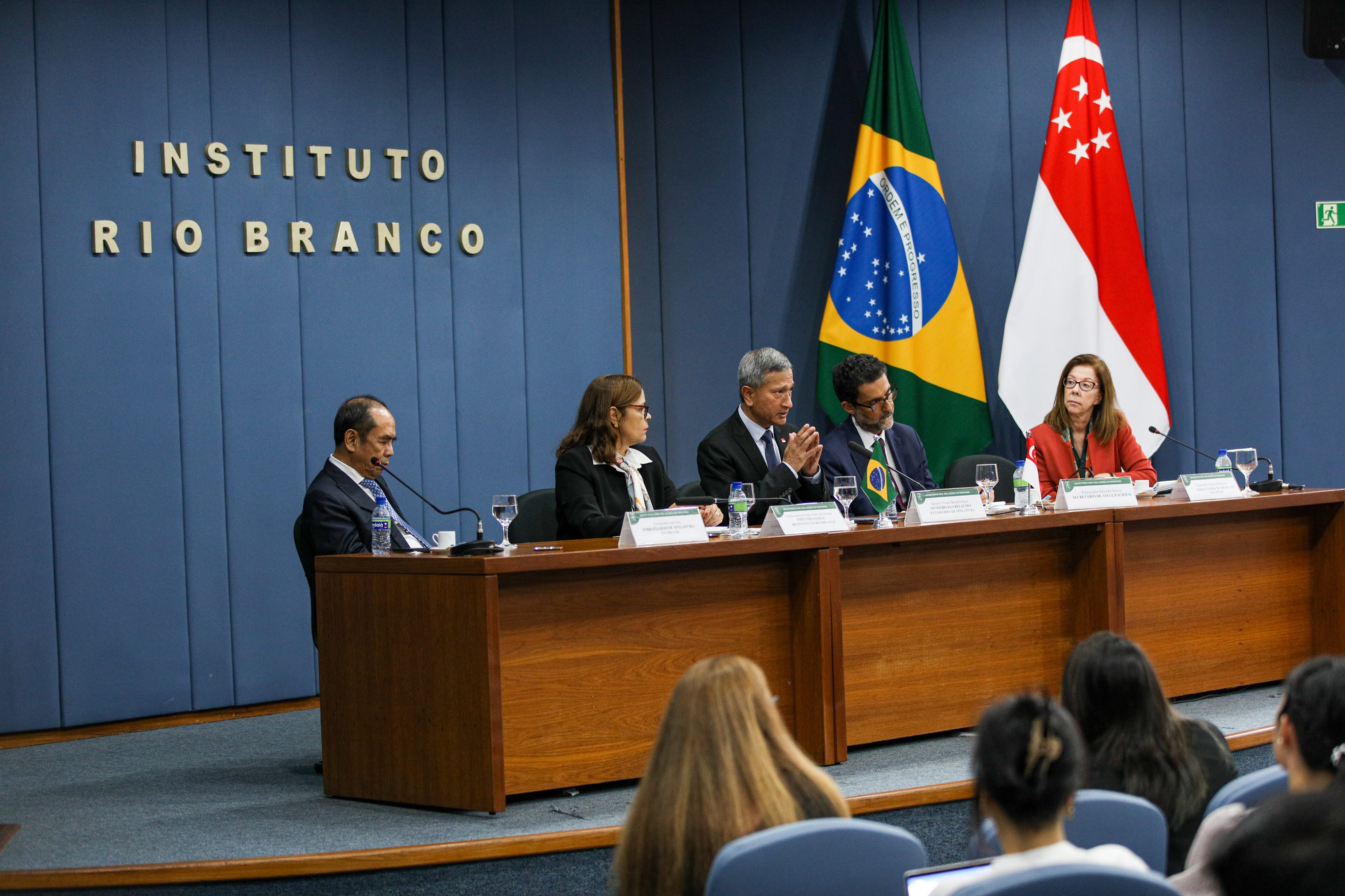 Panel of people at a table with Brazilian and Singapore flags. "Instituto Rio Branco" on wall.
